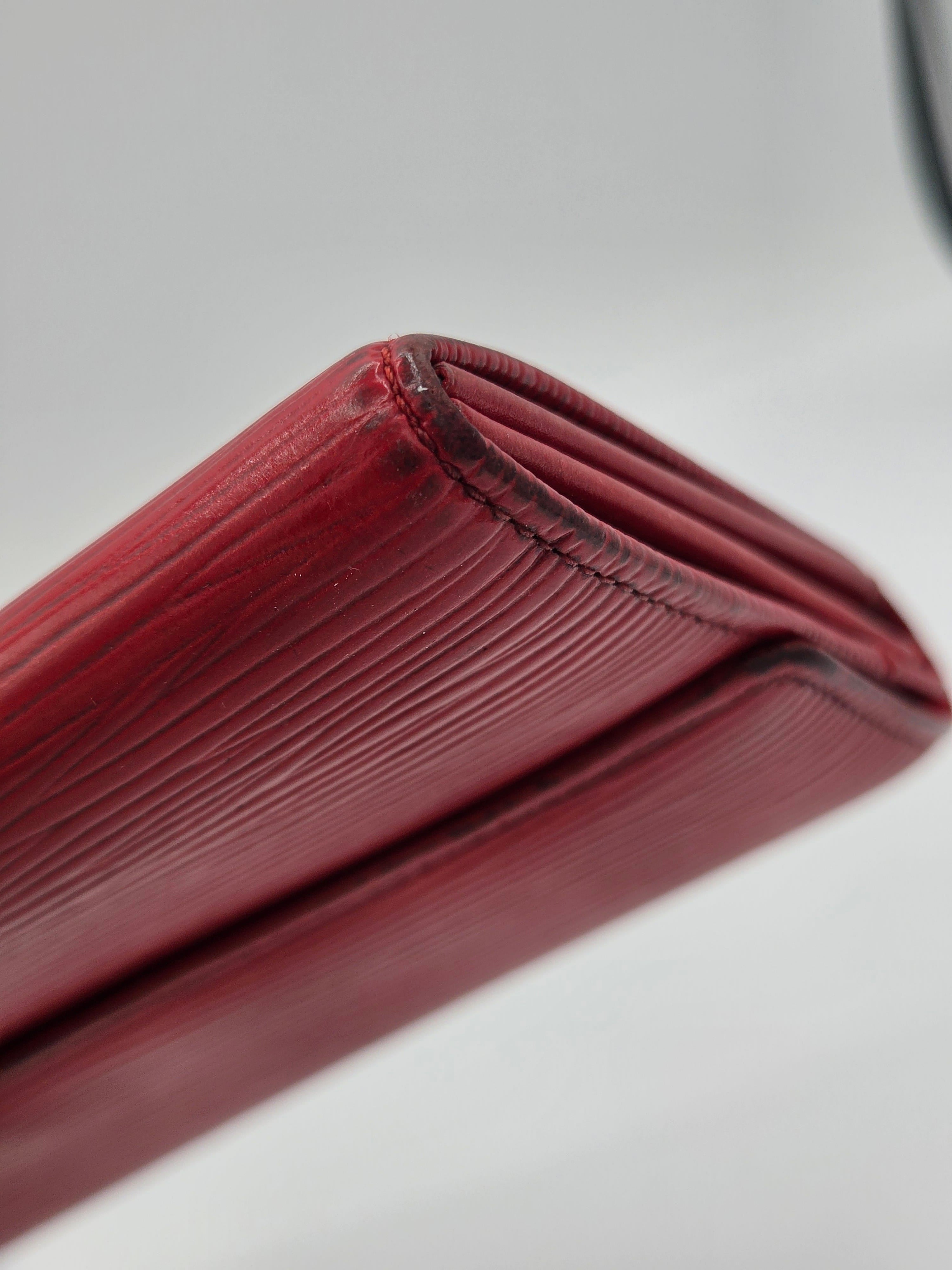A close-up shot of a dark red textured leather wallet, showing the fine grain and stitching against a light gray background.