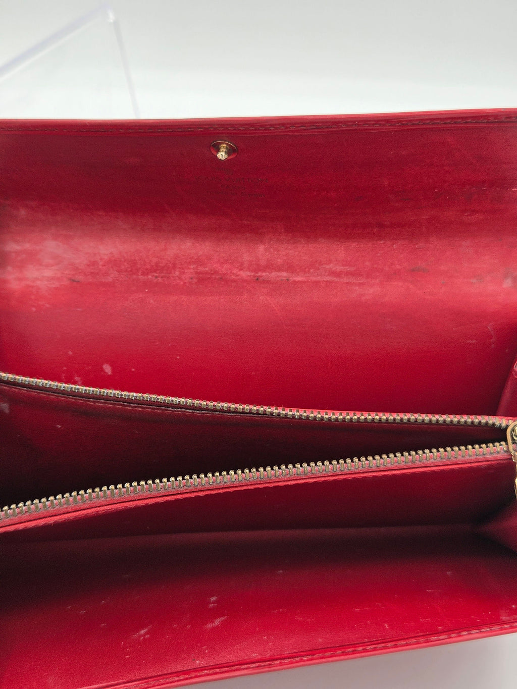 Close-up of a red leather clutch or wallet with a gold-tone zipper and a small gold rivet on a white background.