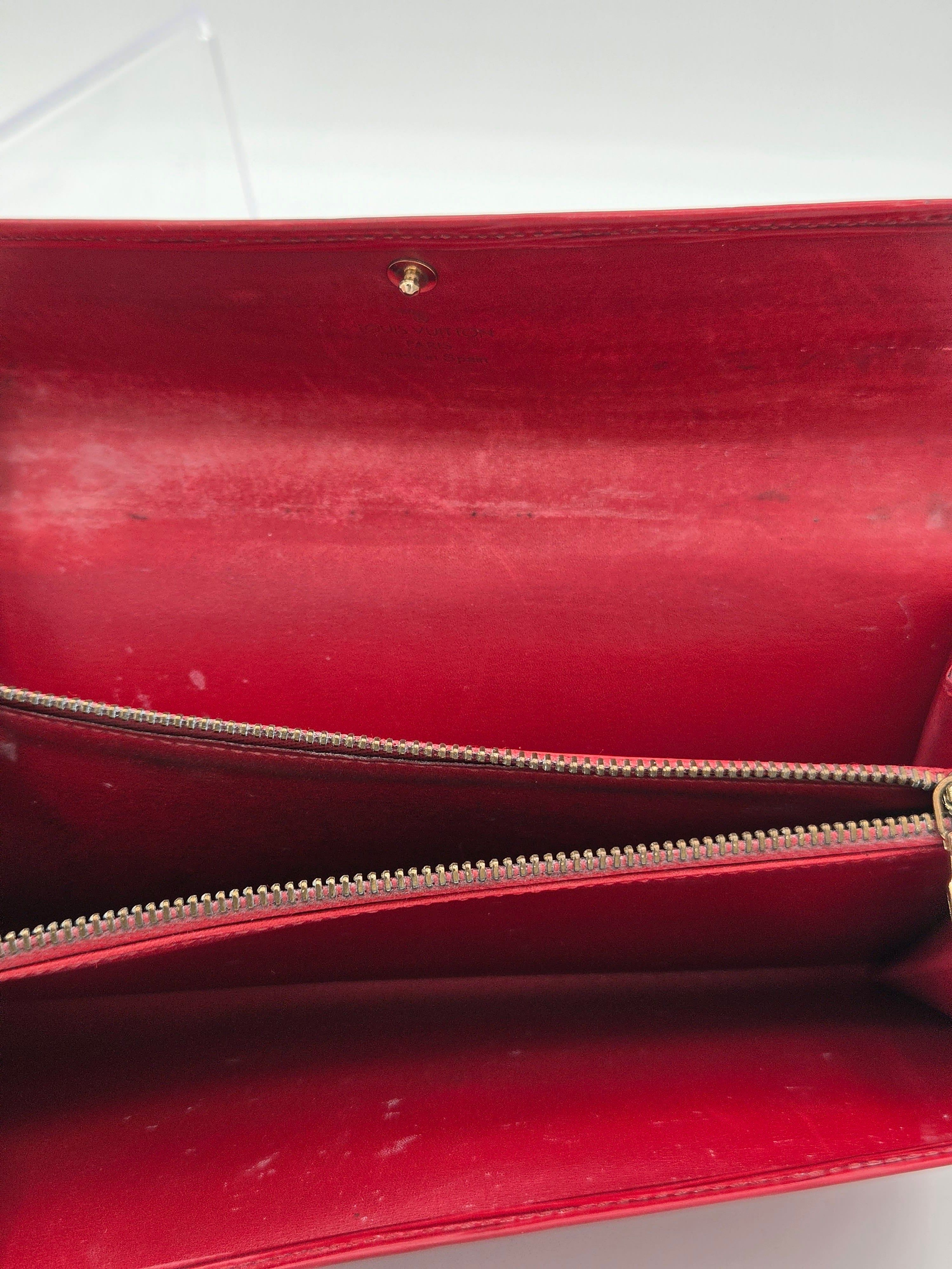 Close-up of a red leather clutch or wallet with a gold-tone zipper and a small gold rivet on a white background.