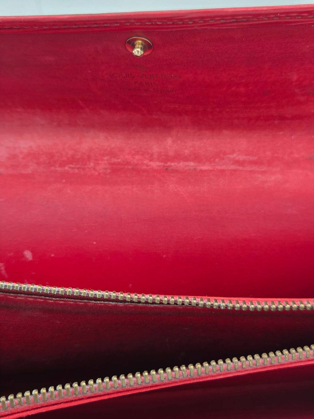 Close-up of a red leather or faux-leather bag interior with a gold-tone zipper and a small gold snap button.