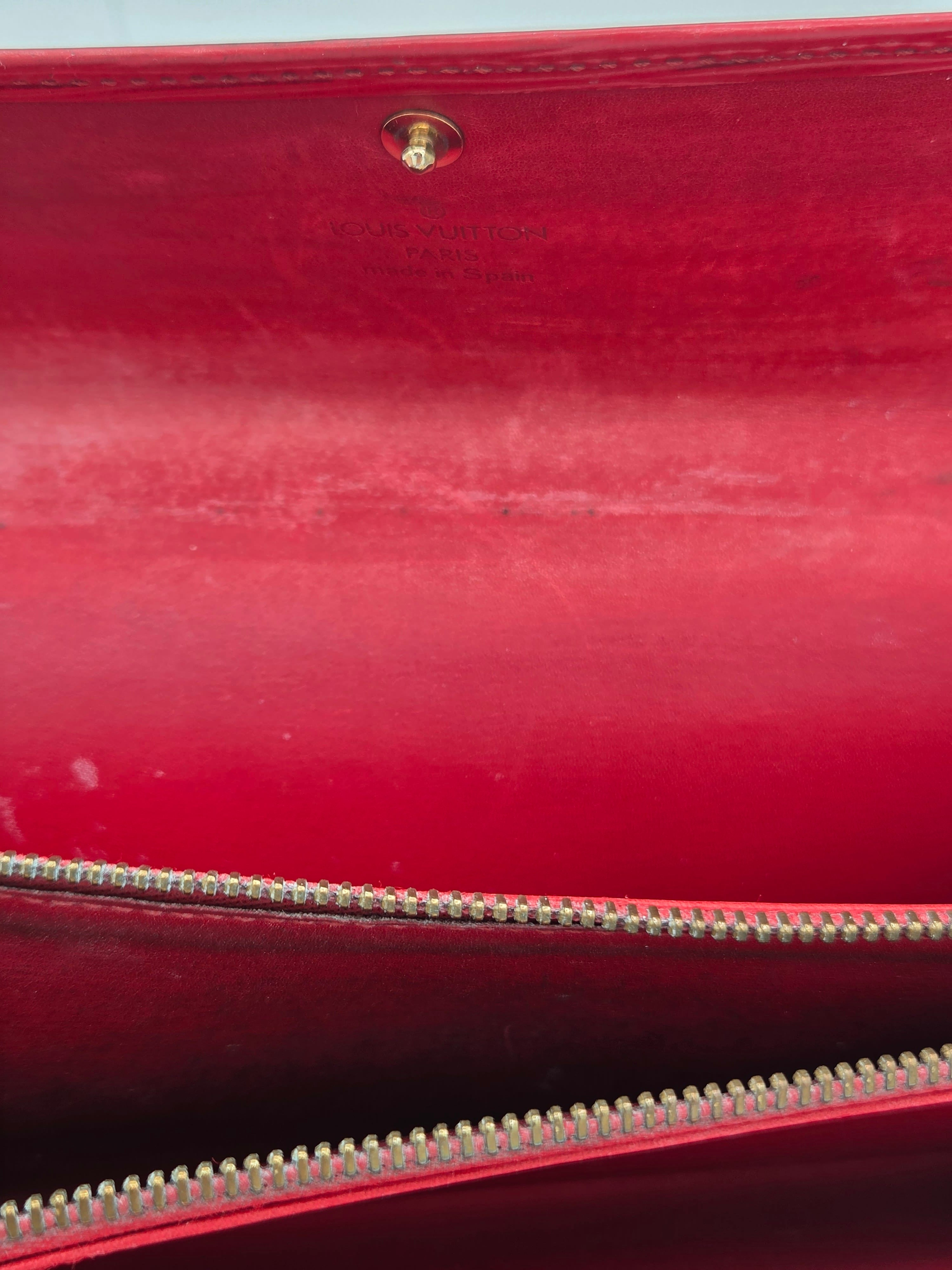 Close-up of a red leather or faux-leather bag interior with a gold-tone zipper and a small gold snap button.