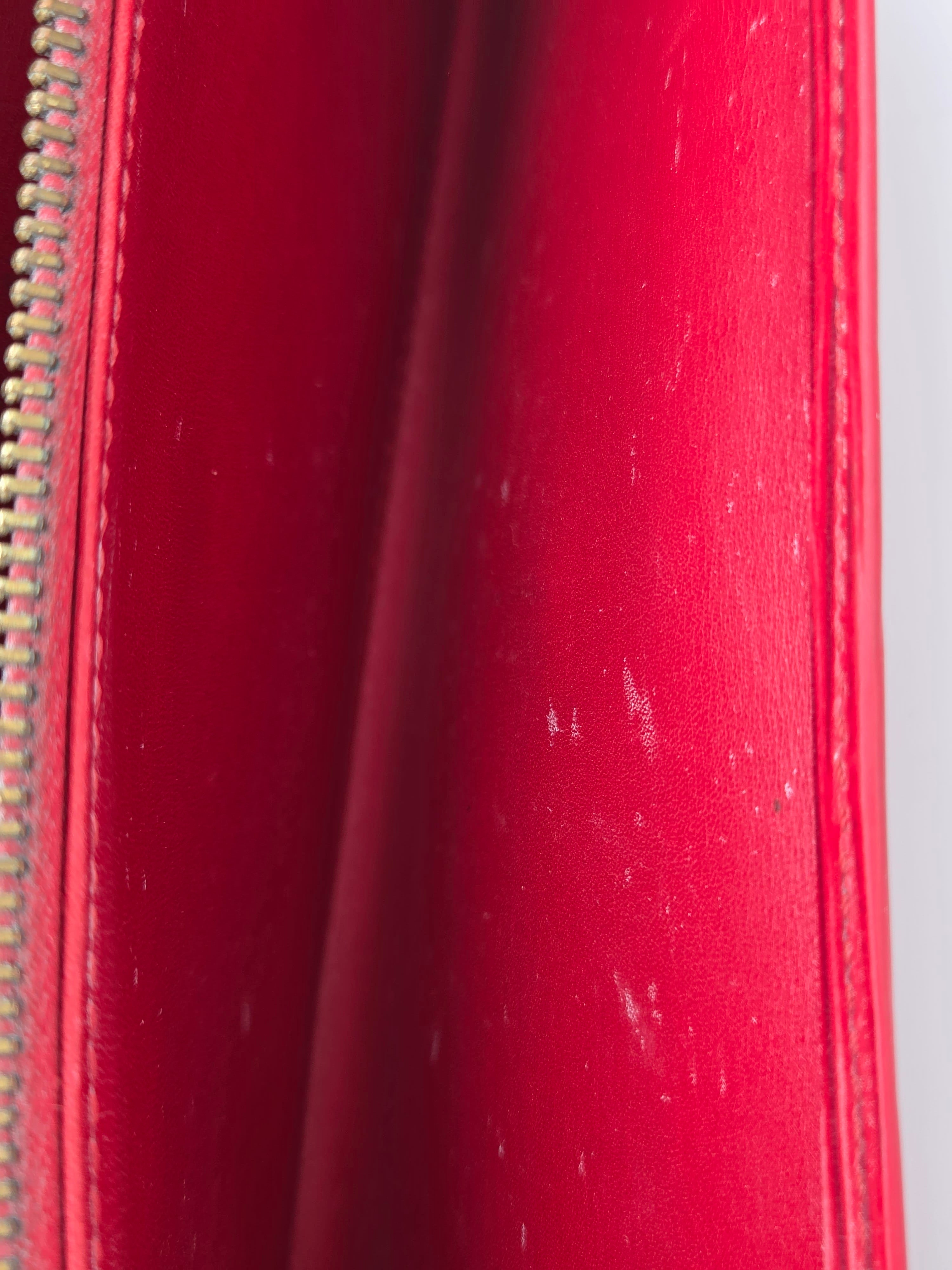Close-up of a red leather zippered pouch or wallet showing the interior lining and a gold-tone zipper.