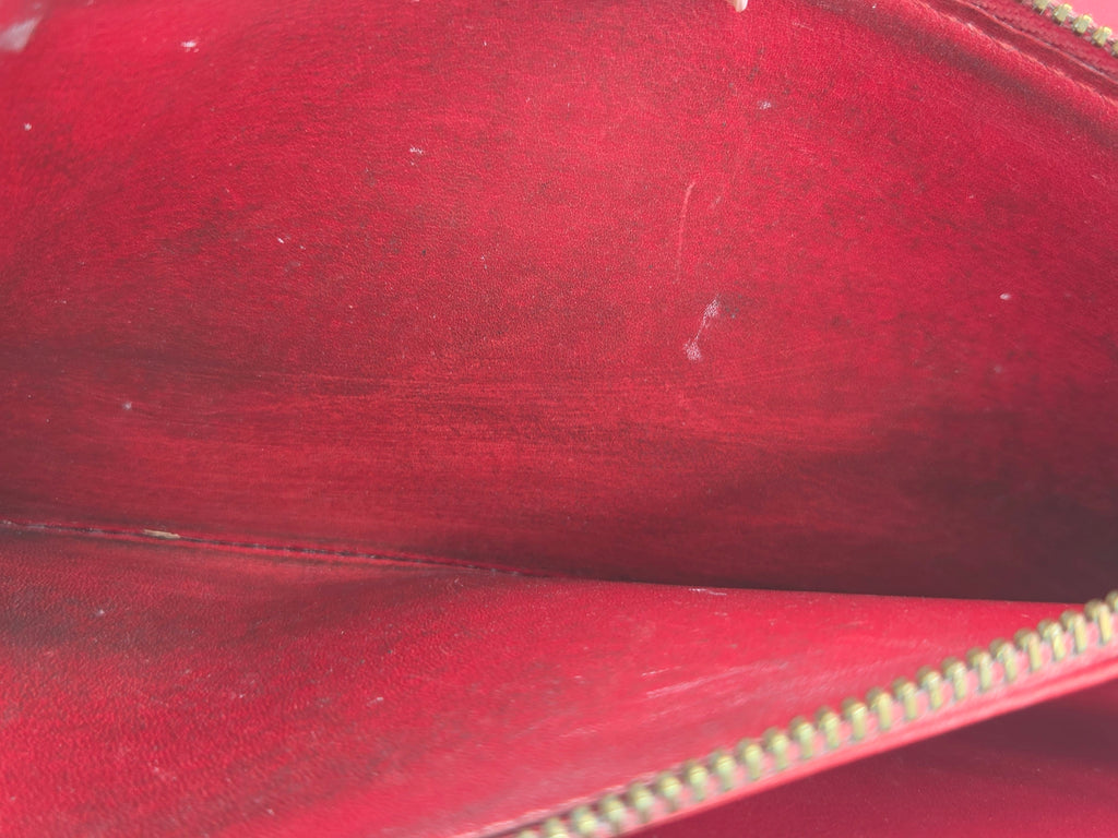 Close-up of the interior lining of a red leather zippered pouch or wallet, showing the red suede-like interior surface and a gold-toned zipper.