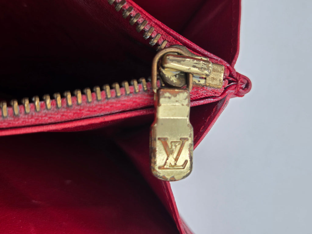 Close-up of a red leather zipper with a gold-tone metal pull featuring an embossed LV logo, indicating Louis Vuitton.