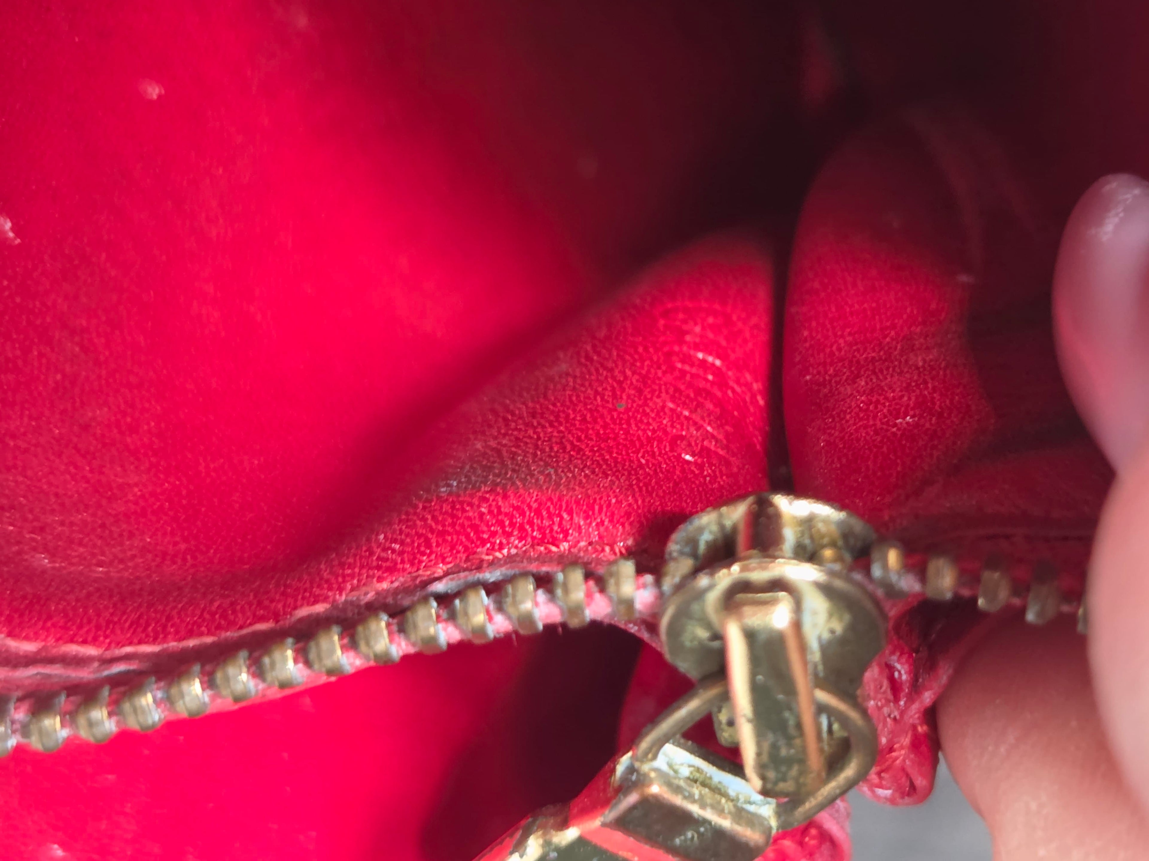 Close-up of a red leather zipper with gold-toned metal teeth and pull, held open by a hand.