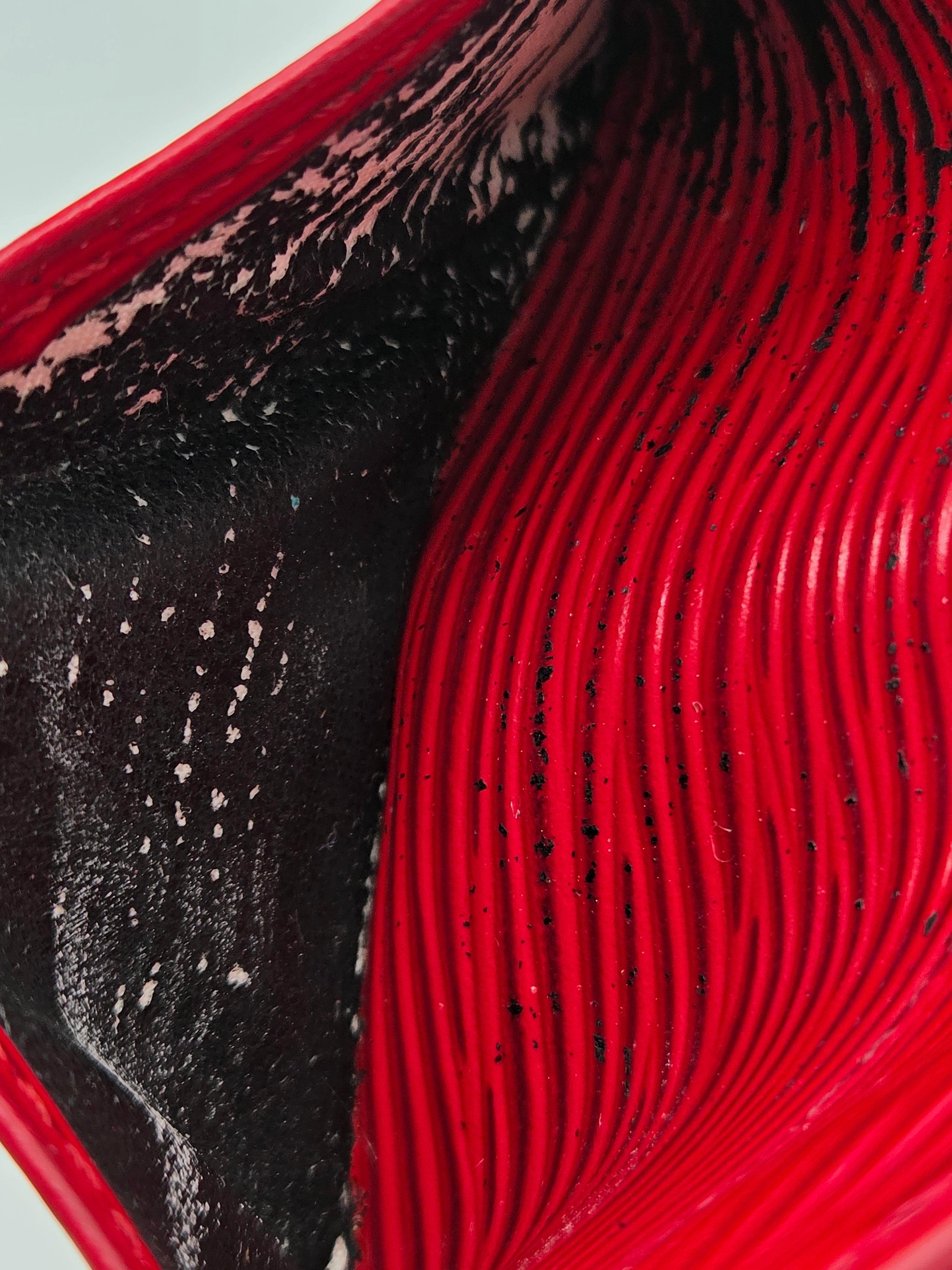 Close-up of a red wavy textured surface with a dark black interior showing white speckles and fine dark lines.