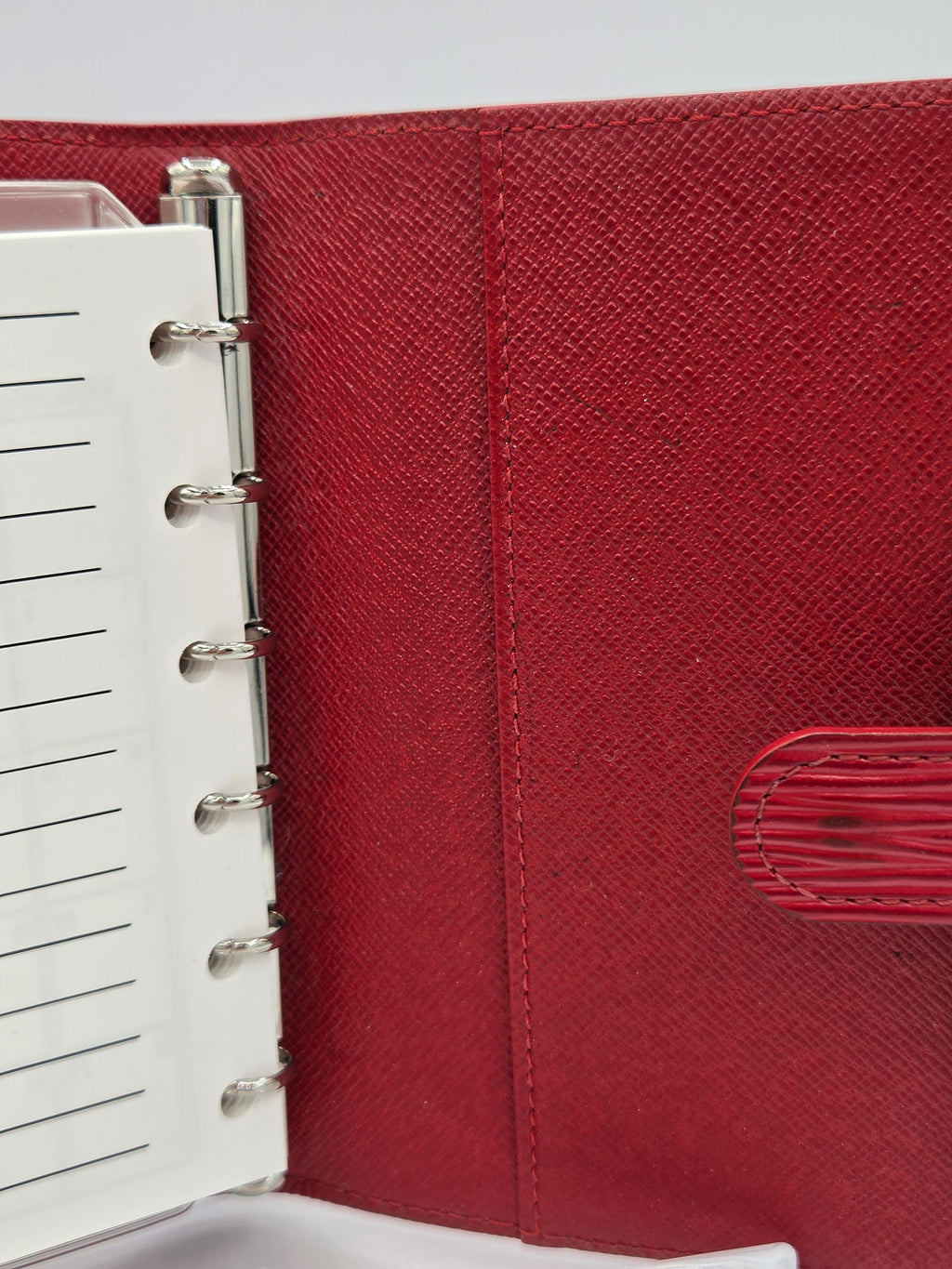 A close-up of a red textured ring binder notebook cover with a white lined page inserted and silver metal rings, photographed against a light background.
