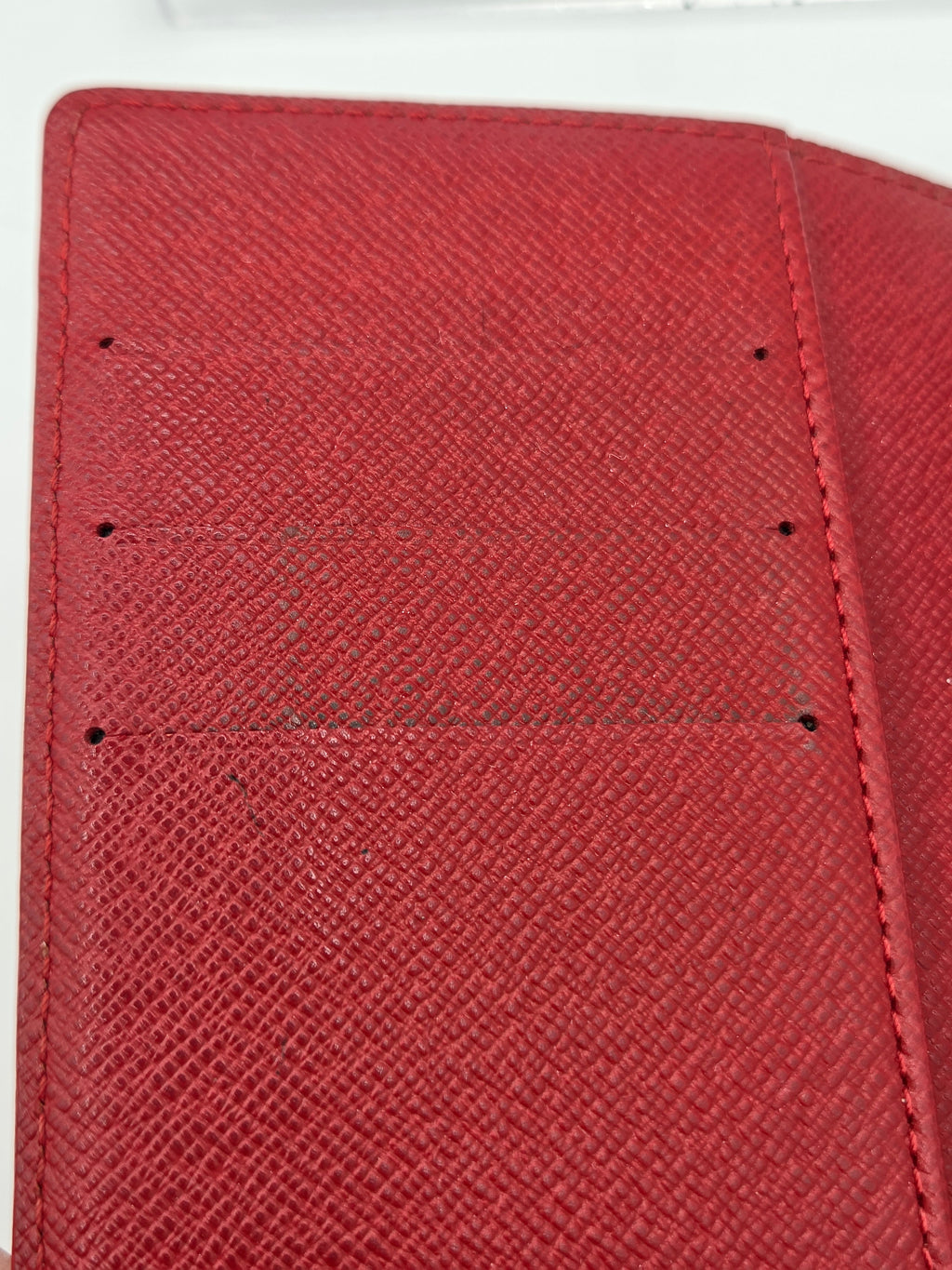 Close-up of a red textured leather wallet or card holder showing the interior lining with stitched compartments and small holes.