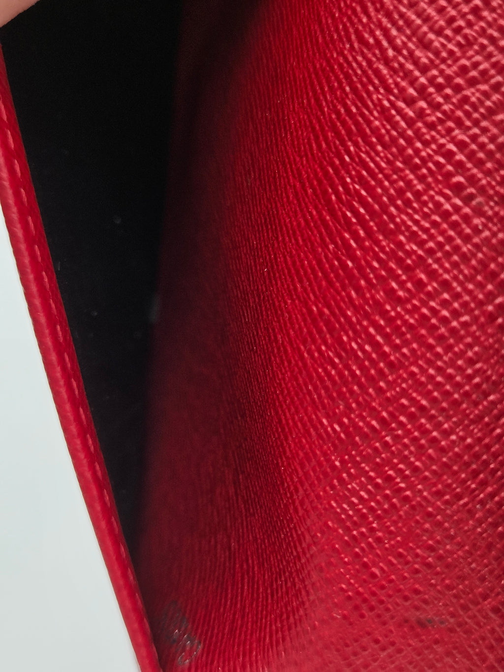Close-up of a red textured leather wallet or clutch showing the interior opening and stitched edge.