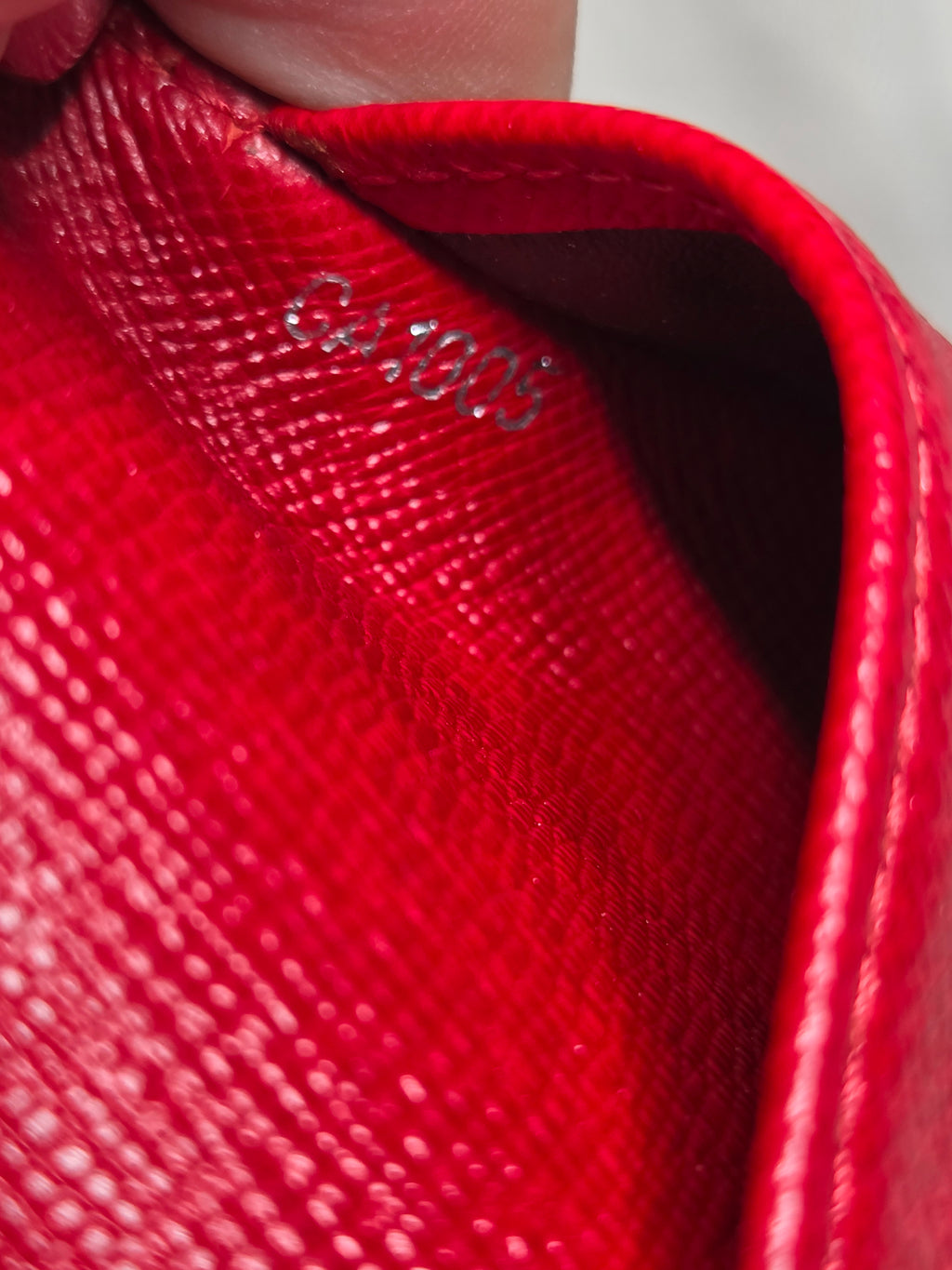Close-up of a bright red textured leather pouch or wallet being held by a hand, showing the interior lining and a small silver stamped logo.