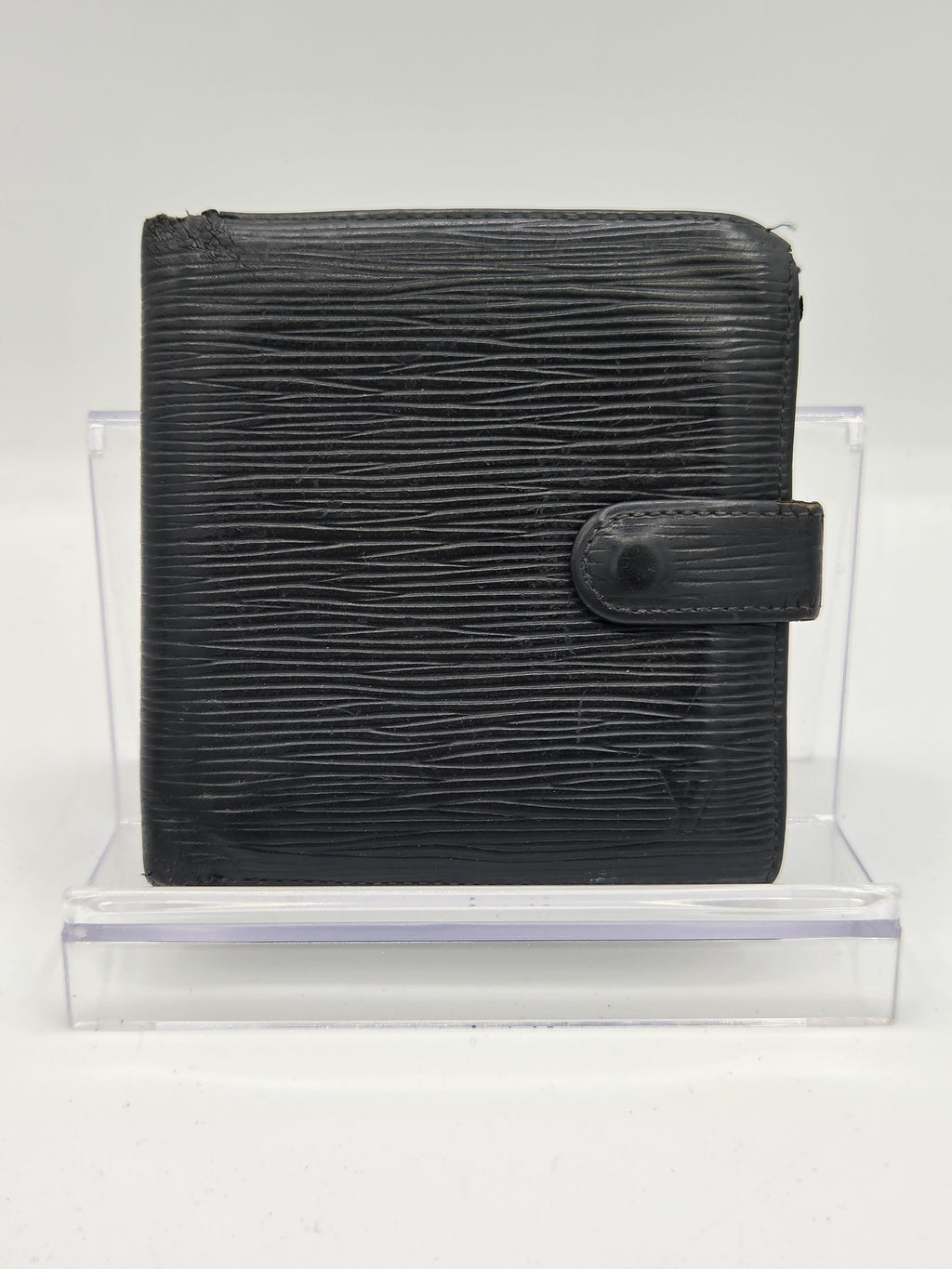 A black textured leather bifold wallet with a snap tab closure, displayed inside a clear acrylic block against a white background.