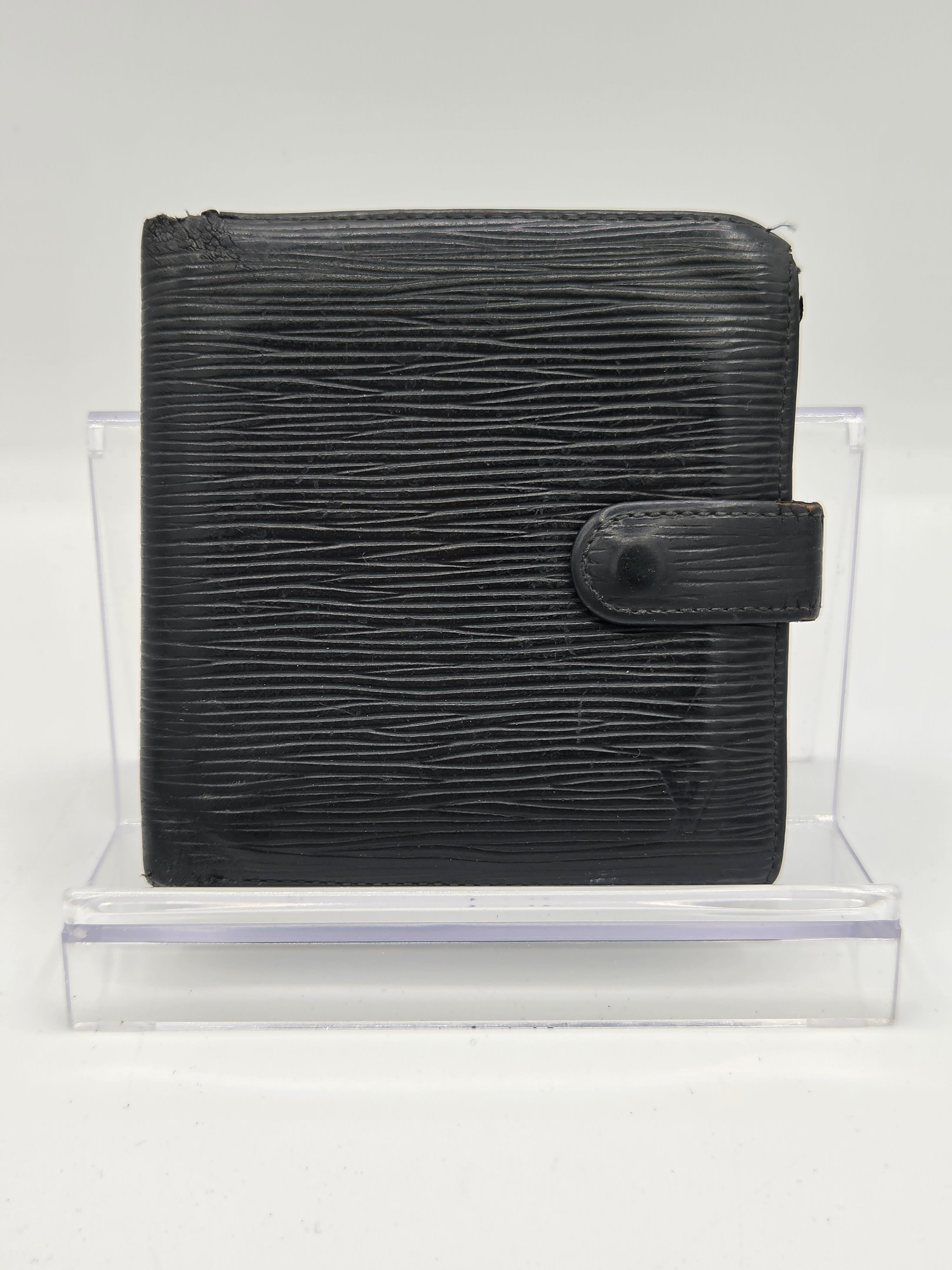 A black textured leather bifold wallet with a snap tab closure, displayed inside a clear acrylic block against a white background.