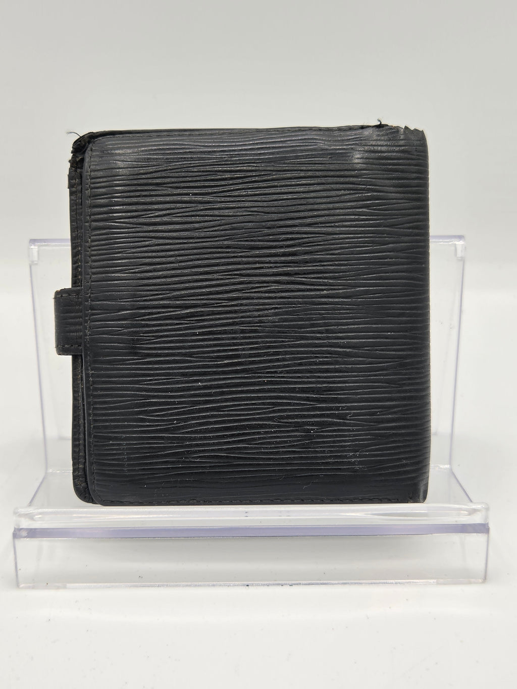 A black textured leather wallet with a vertical grain pattern, displayed on a clear acrylic stand against a white background.