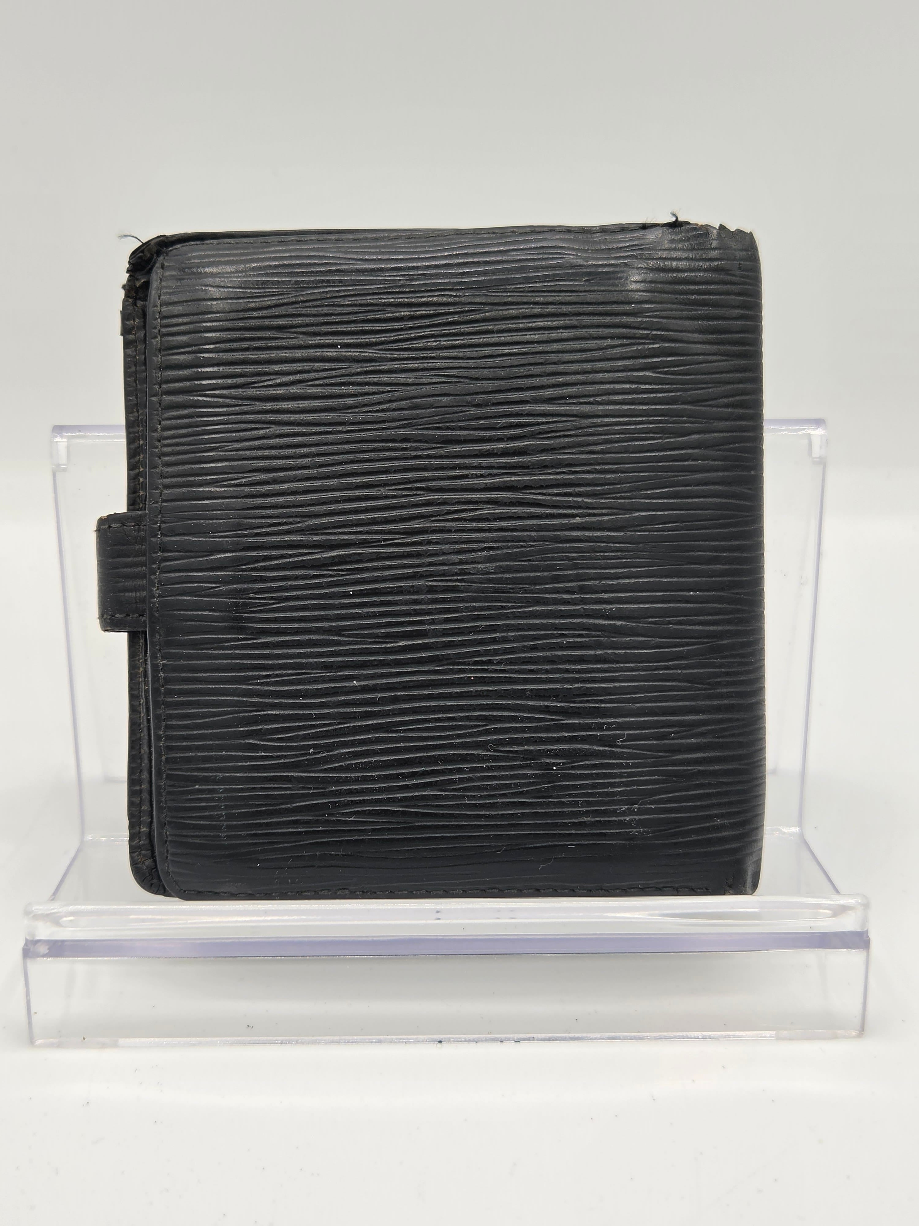 A black textured leather wallet with a vertical grain pattern, displayed on a clear acrylic stand against a white background.