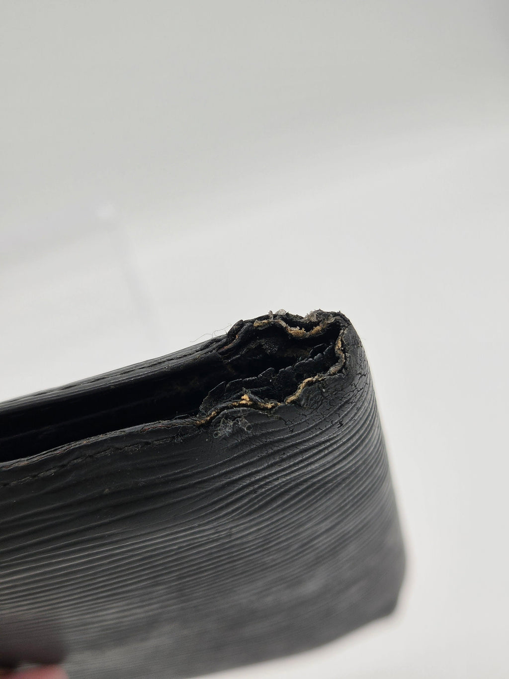 Close-up of a black textured leather wallet corner showing a severely torn and frayed edge against a plain white background.