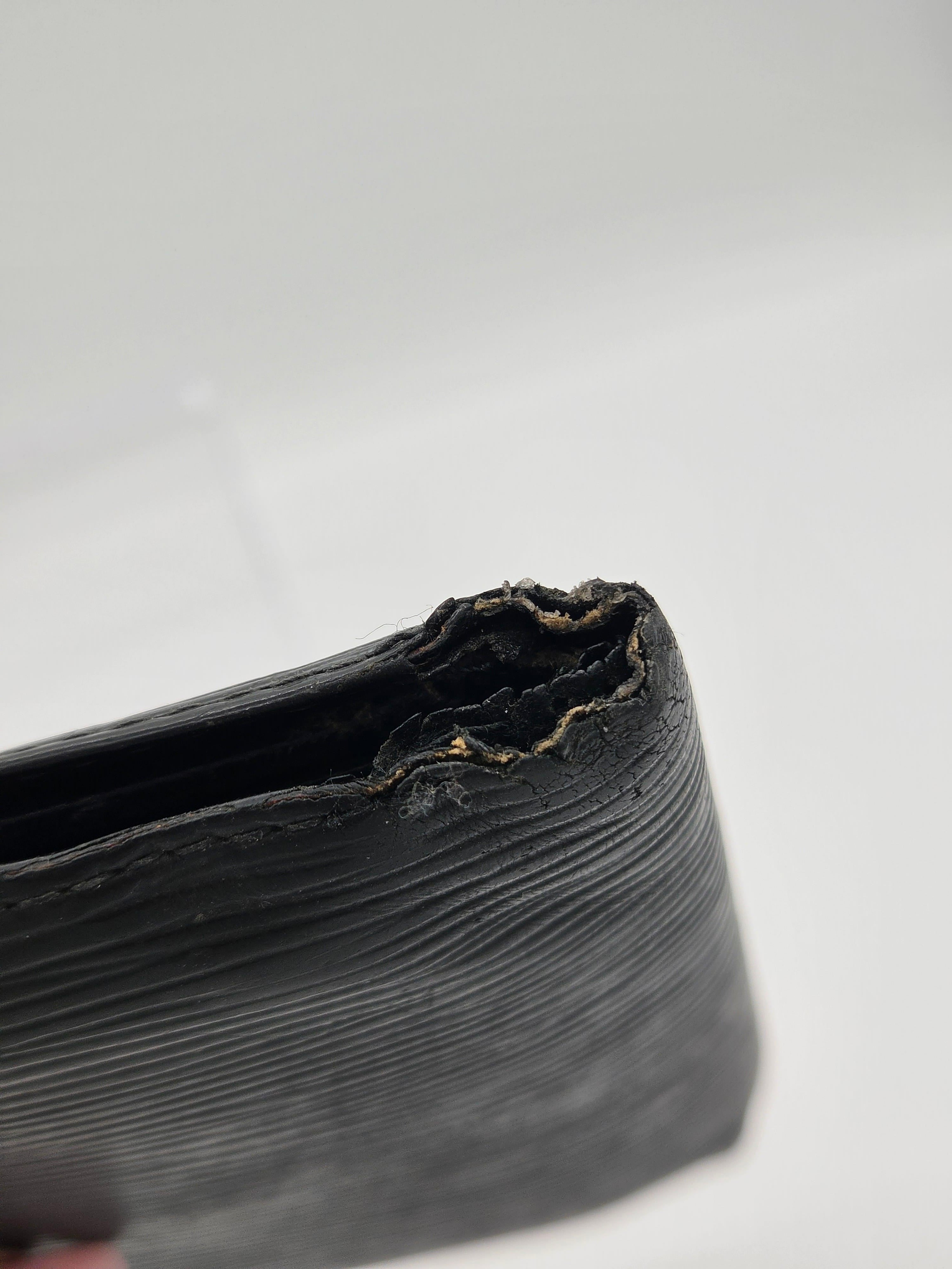 Close-up of a black textured leather wallet corner showing a severely torn and frayed edge against a plain white background.