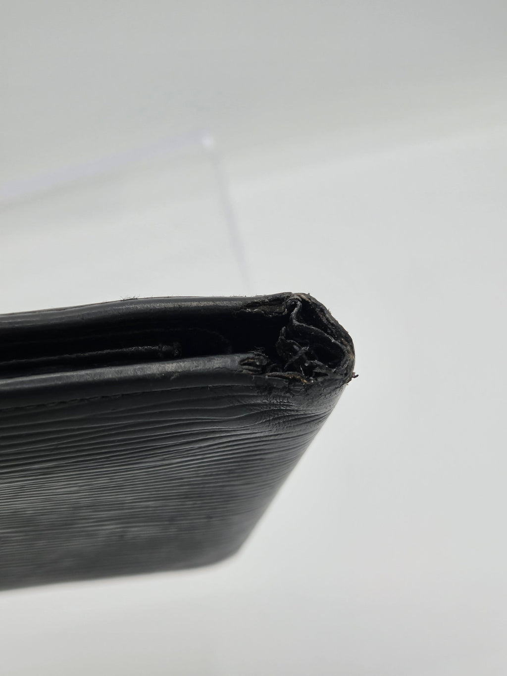 A close-up of a black textured leather wallet or folio showing a heavily damaged, frayed, and chewed edge on a plain light gray background.