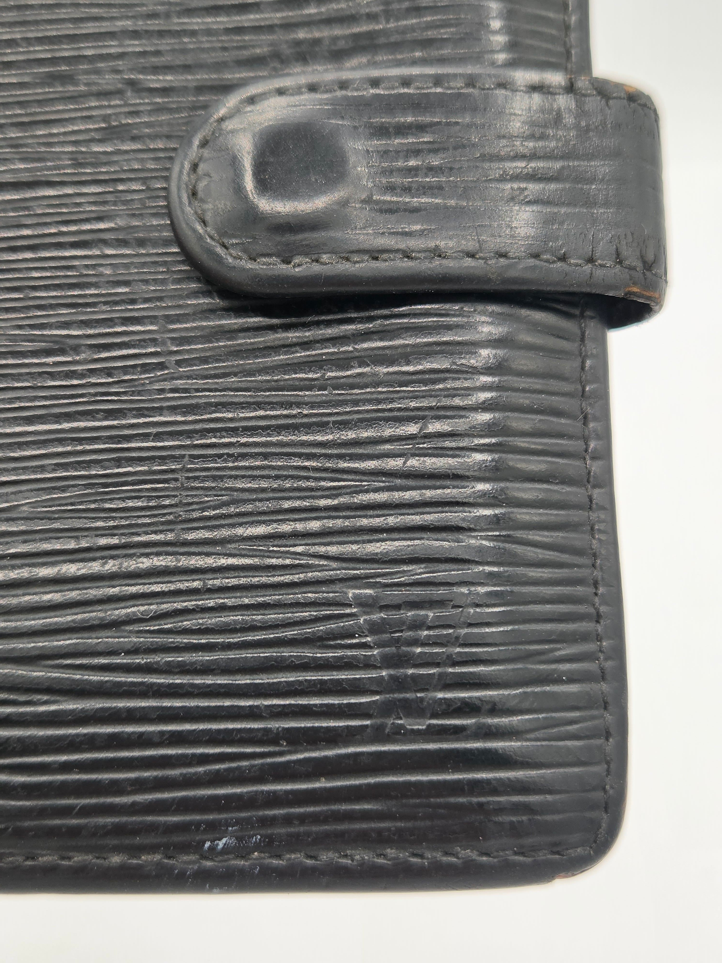Close-up of a dark gray textured leather wallet showing the vertical grain pattern and snap tab closure against a plain white background.