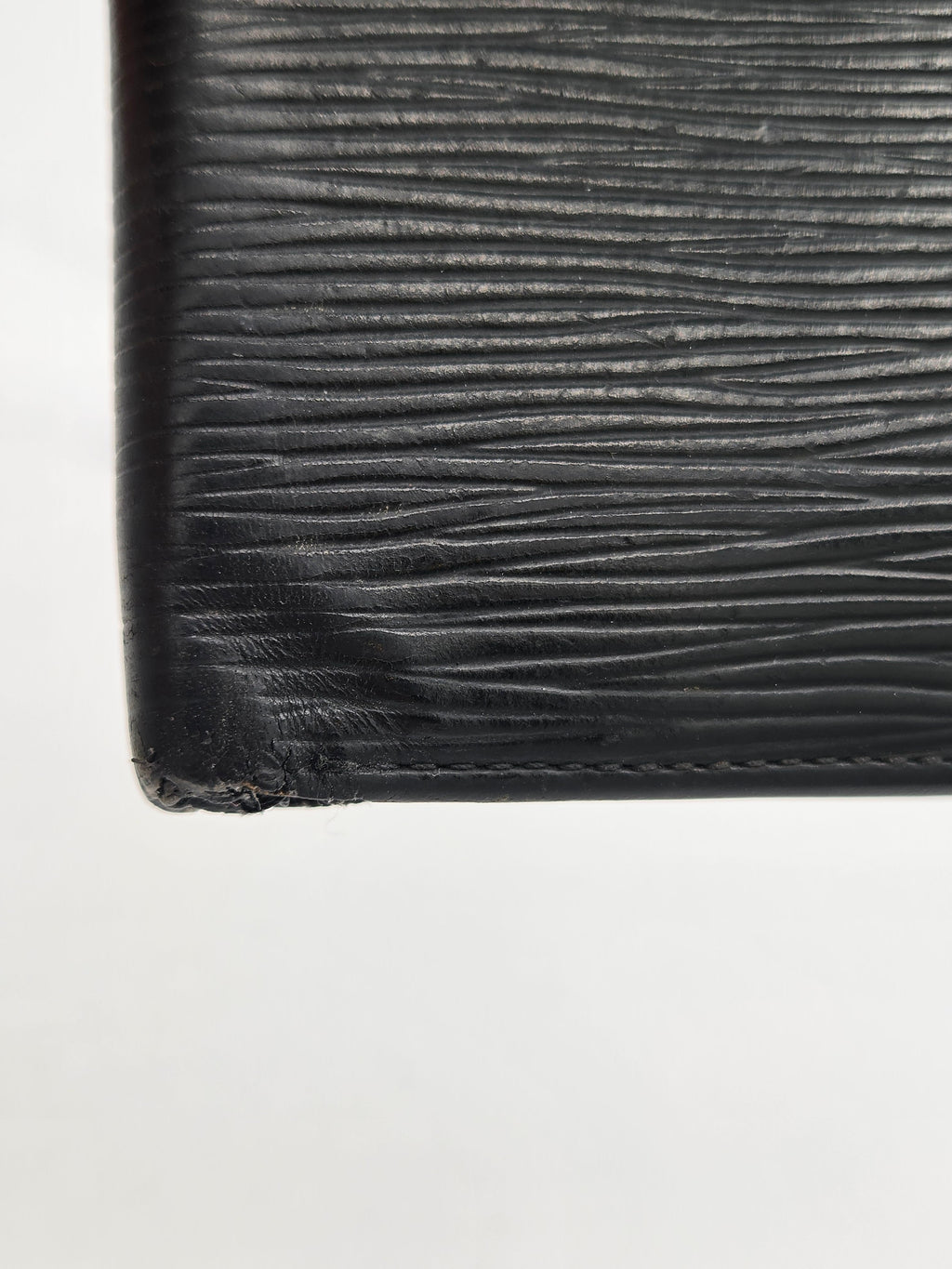 Close-up of a black textured leather item corner with visible wear and frayed edge on a plain white background.