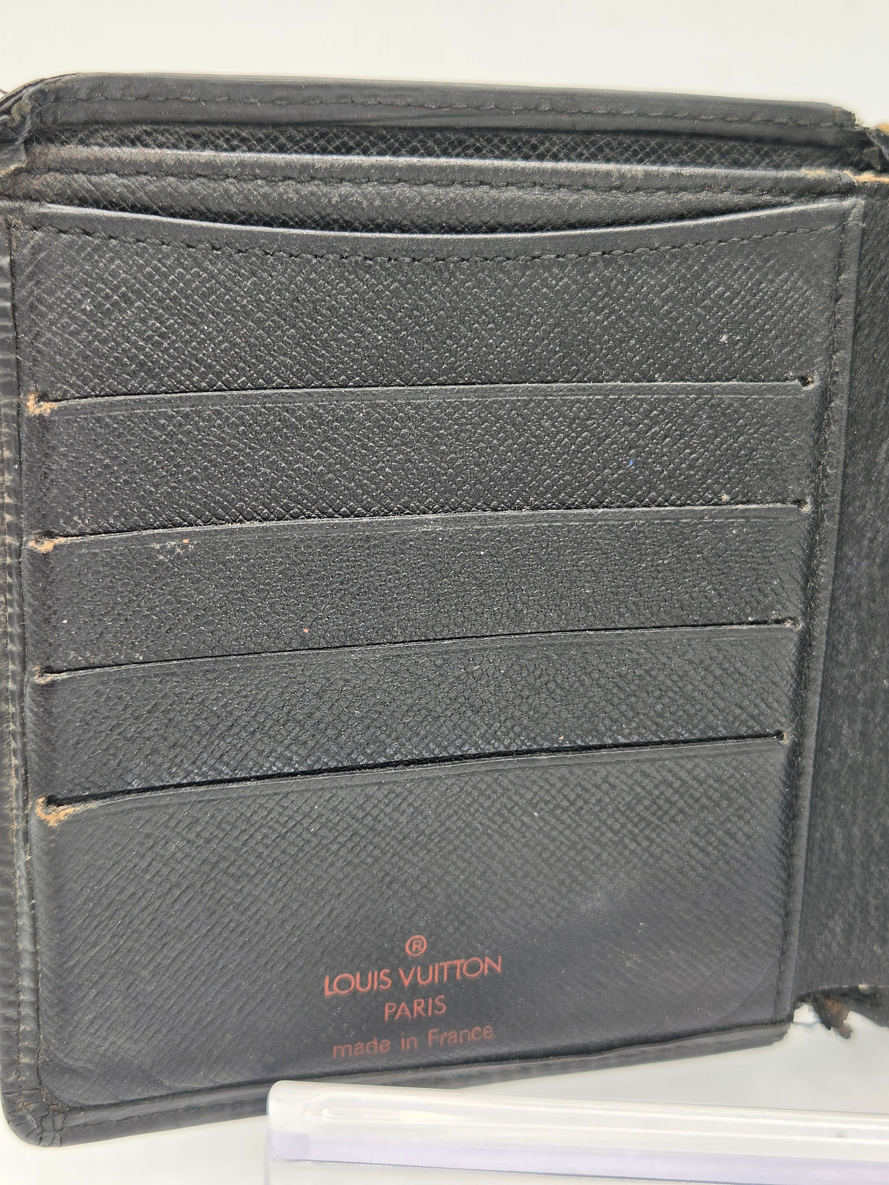 A close-up of a black Louis Vuitton bi-fold wallet made of textured Saffiano leather, showing the interior card slots and the brand's logo printed in red on the bottom left.