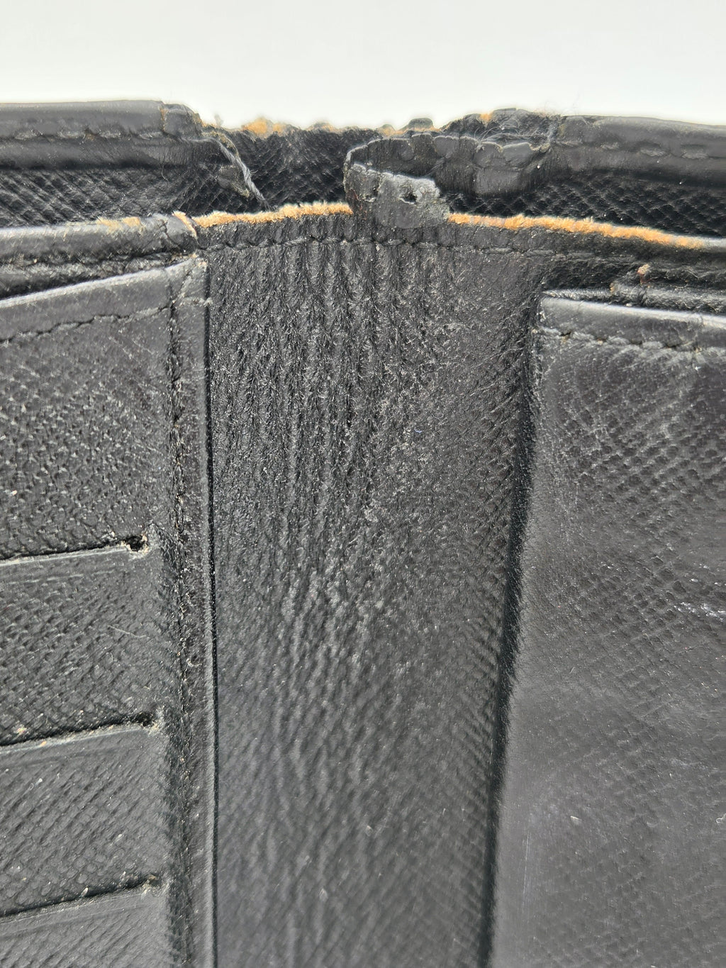 Close-up of a black textured leather wallet showing the interior lining, stitching, and a worn, frayed edge.
