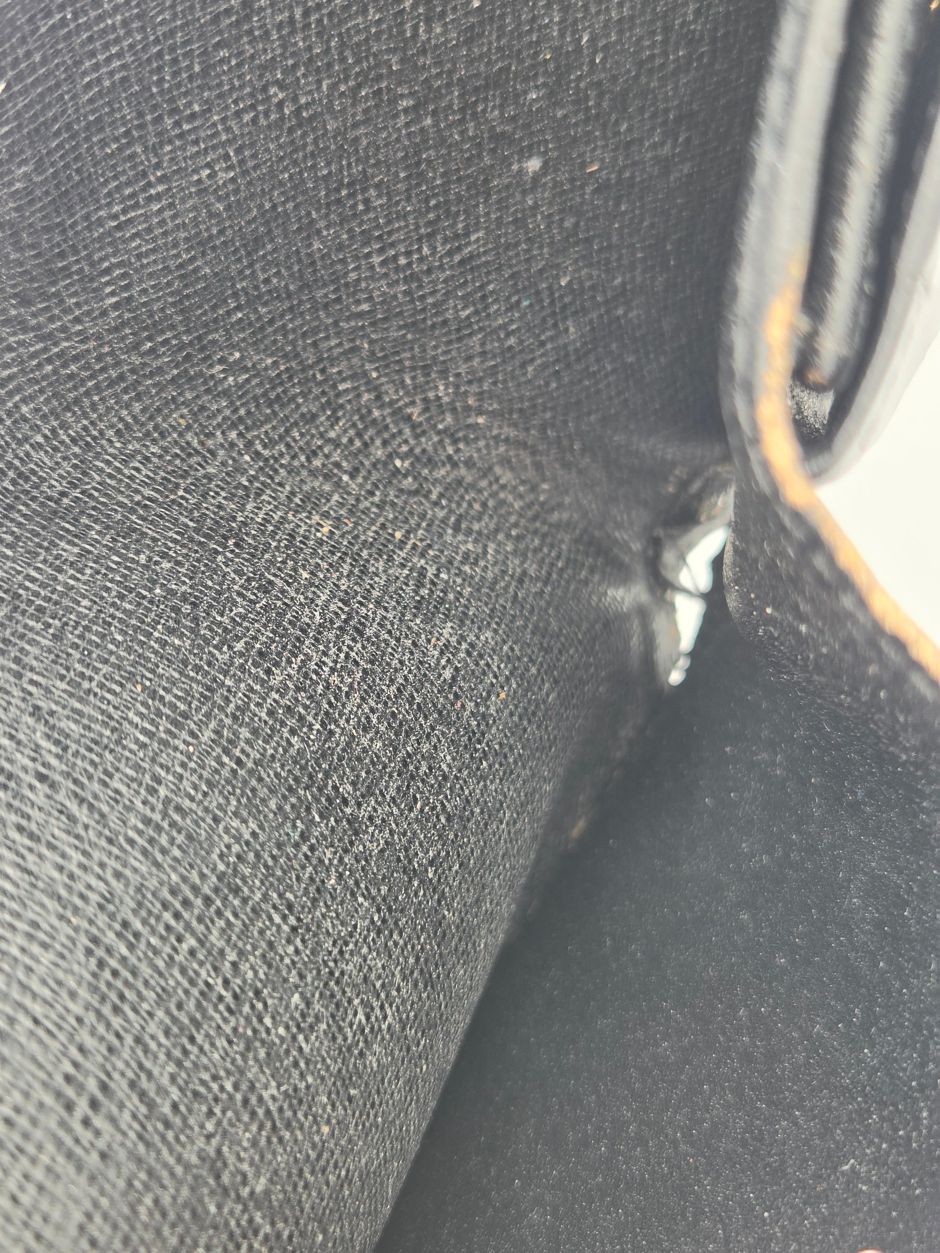 Close-up detail shot of a dark gray woven fabric surface with a black interior corner and a small metallic zipper pull visible.
