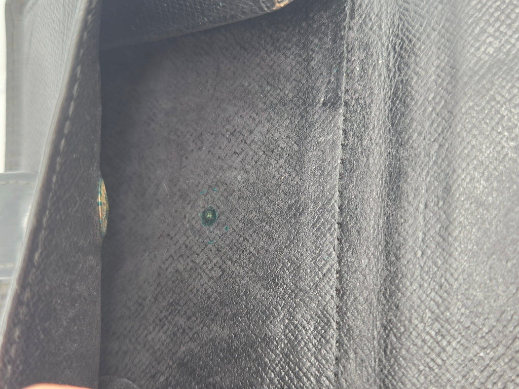 Close-up of a black textured leather or faux-leather interior corner with a small round green gemstone or bead centered on the lining.