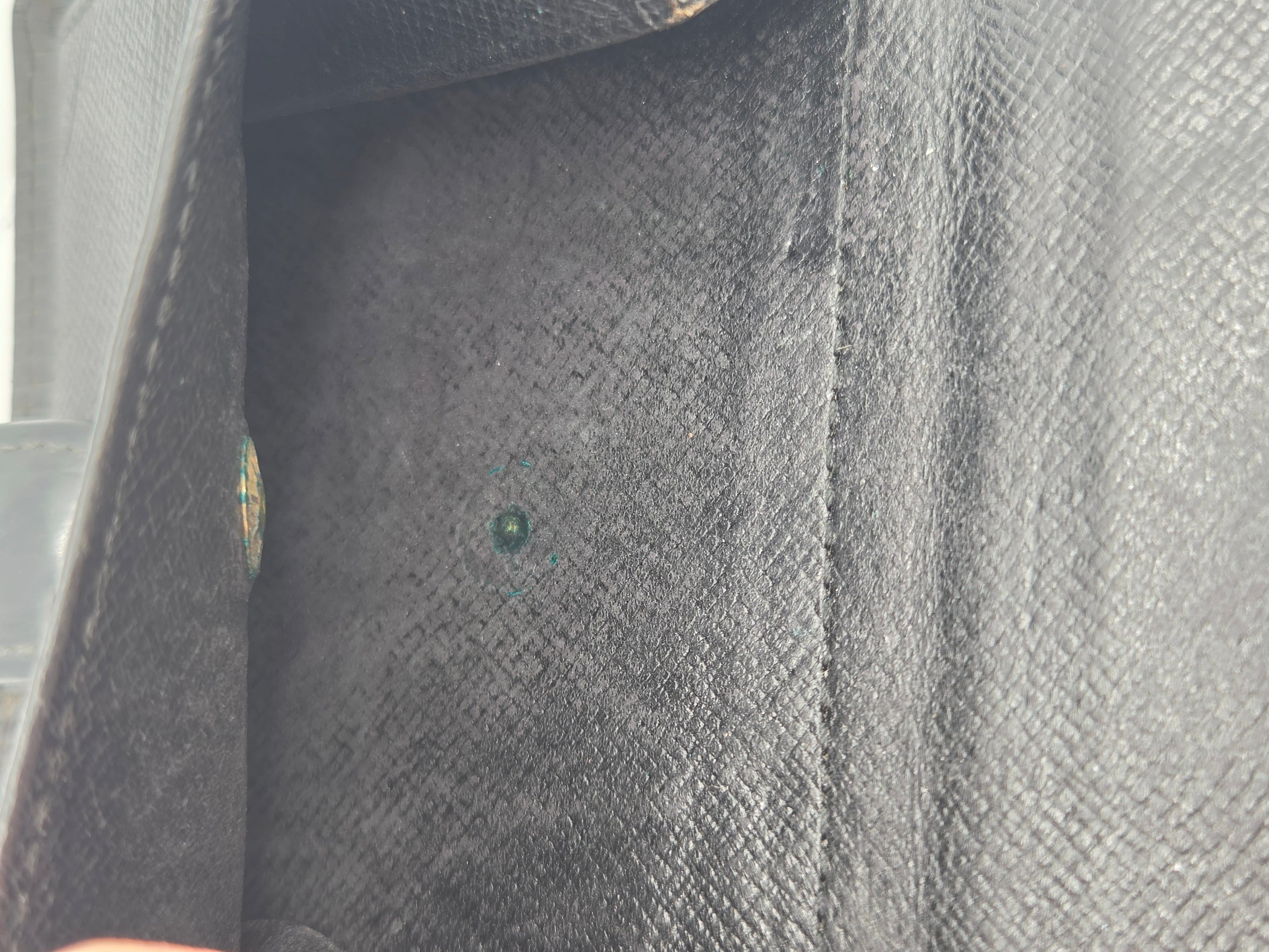 Close-up of a black textured leather or faux-leather interior corner with a small round green gemstone or bead centered on the lining.