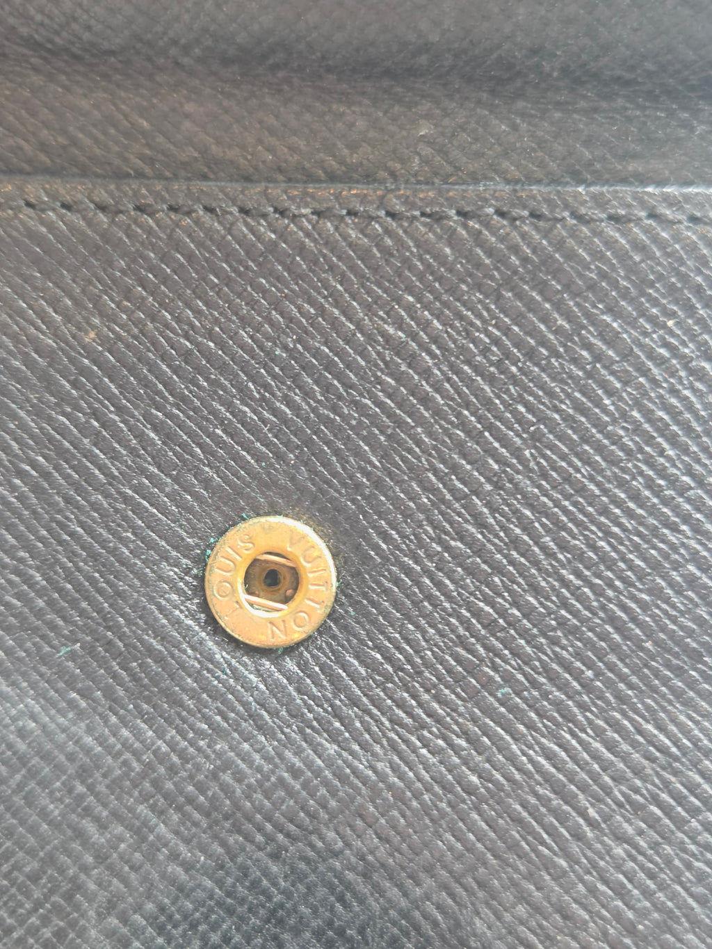 Close-up of a dark gray textured fabric with a small gold-toned metal snap button on the right side.