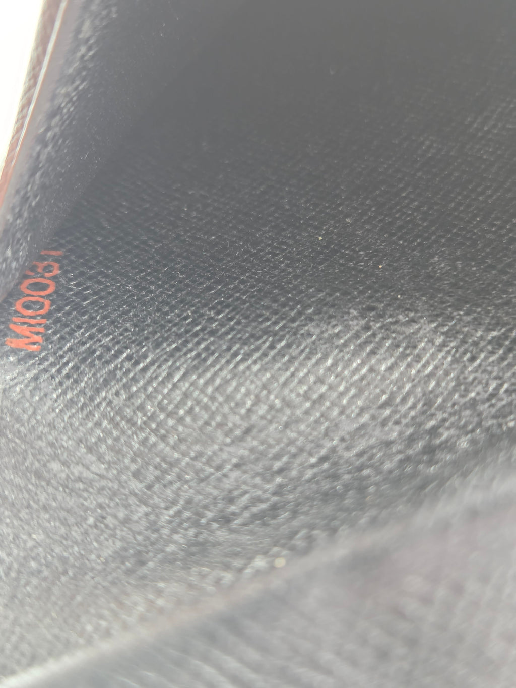 Close-up of a textured black leather surface with a small orange printed marking near the bottom.
