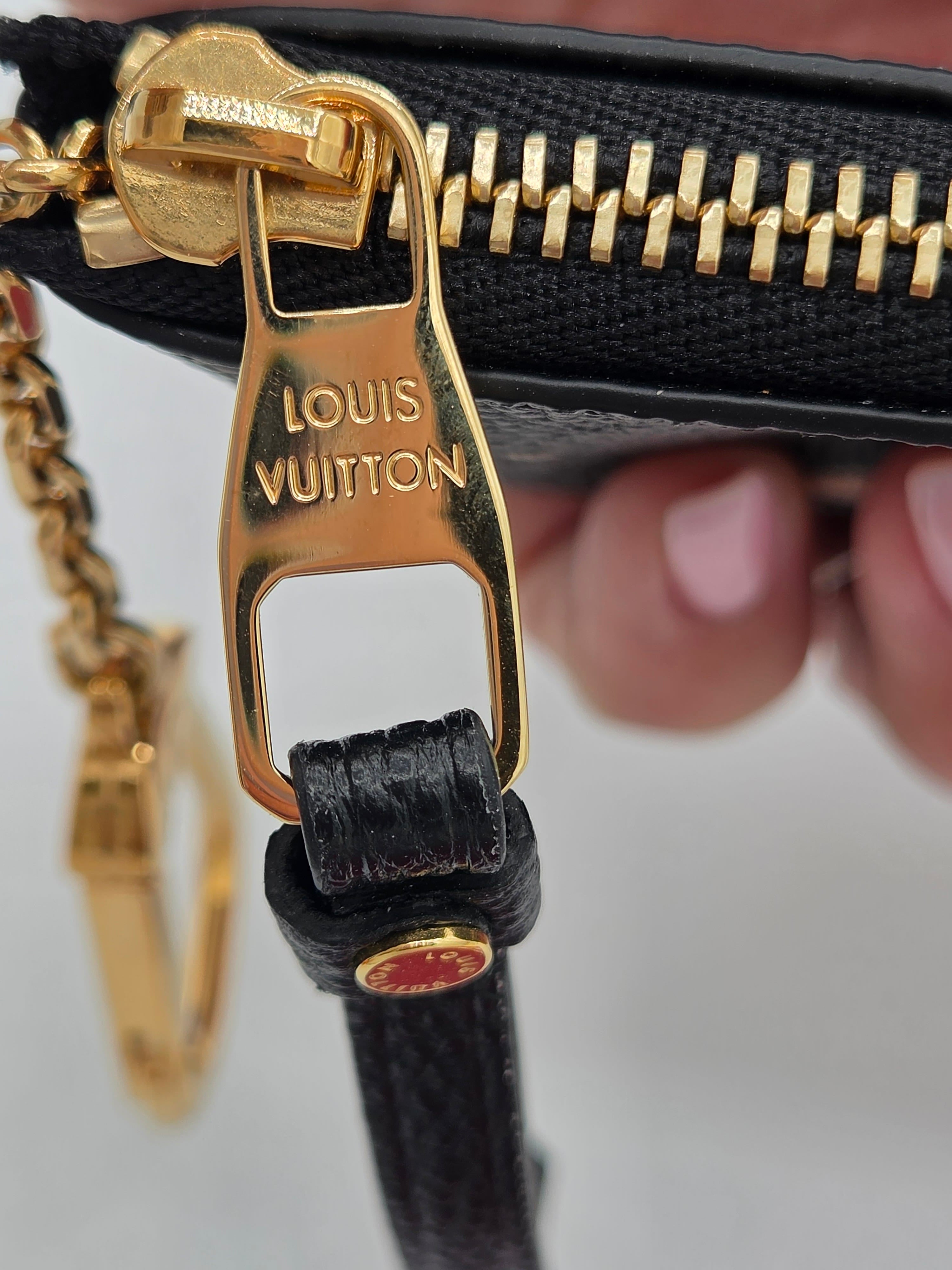 Close-up of a Louis Vuitton black leather wristlet or pouch with a gold-tone zipper pull engraved with 'LOUIS VUITTON', held by a hand.