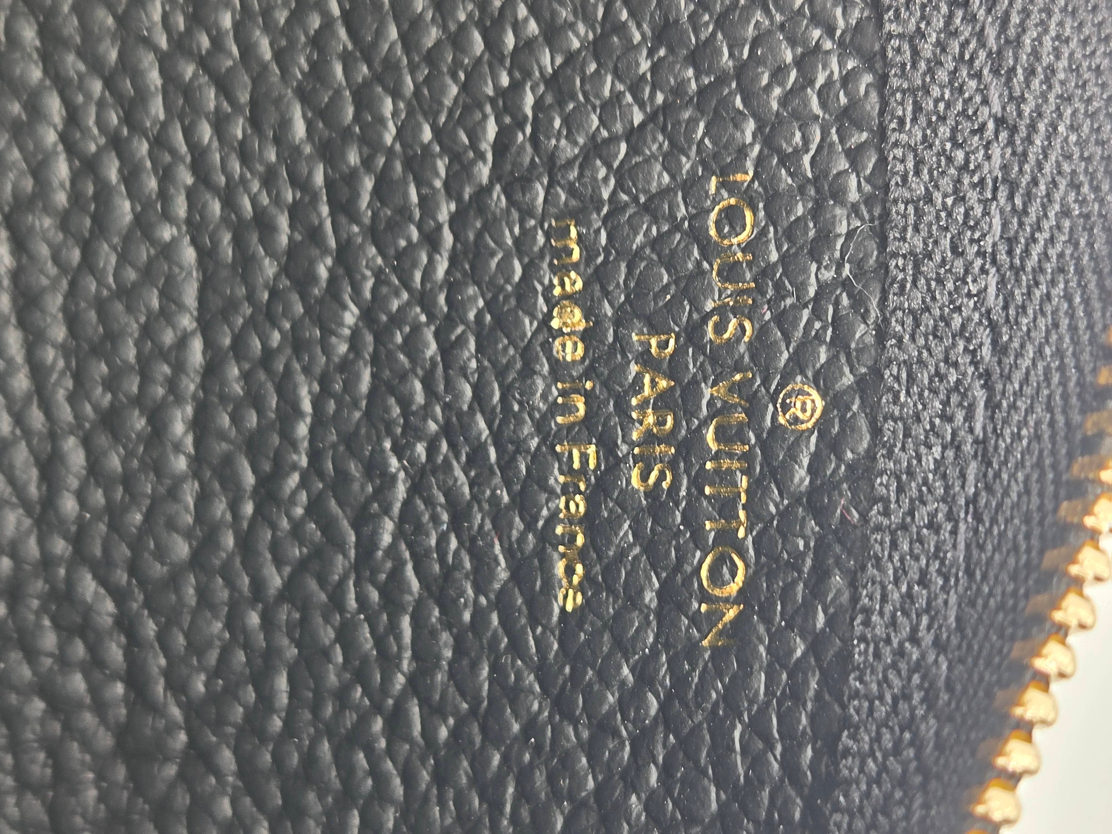 Close-up of a Louis Vuitton black pebbled leather item with gold foil stamping reading 'Louis Vuitton Paris Made in France' and a gold zipper edge visible on the right.