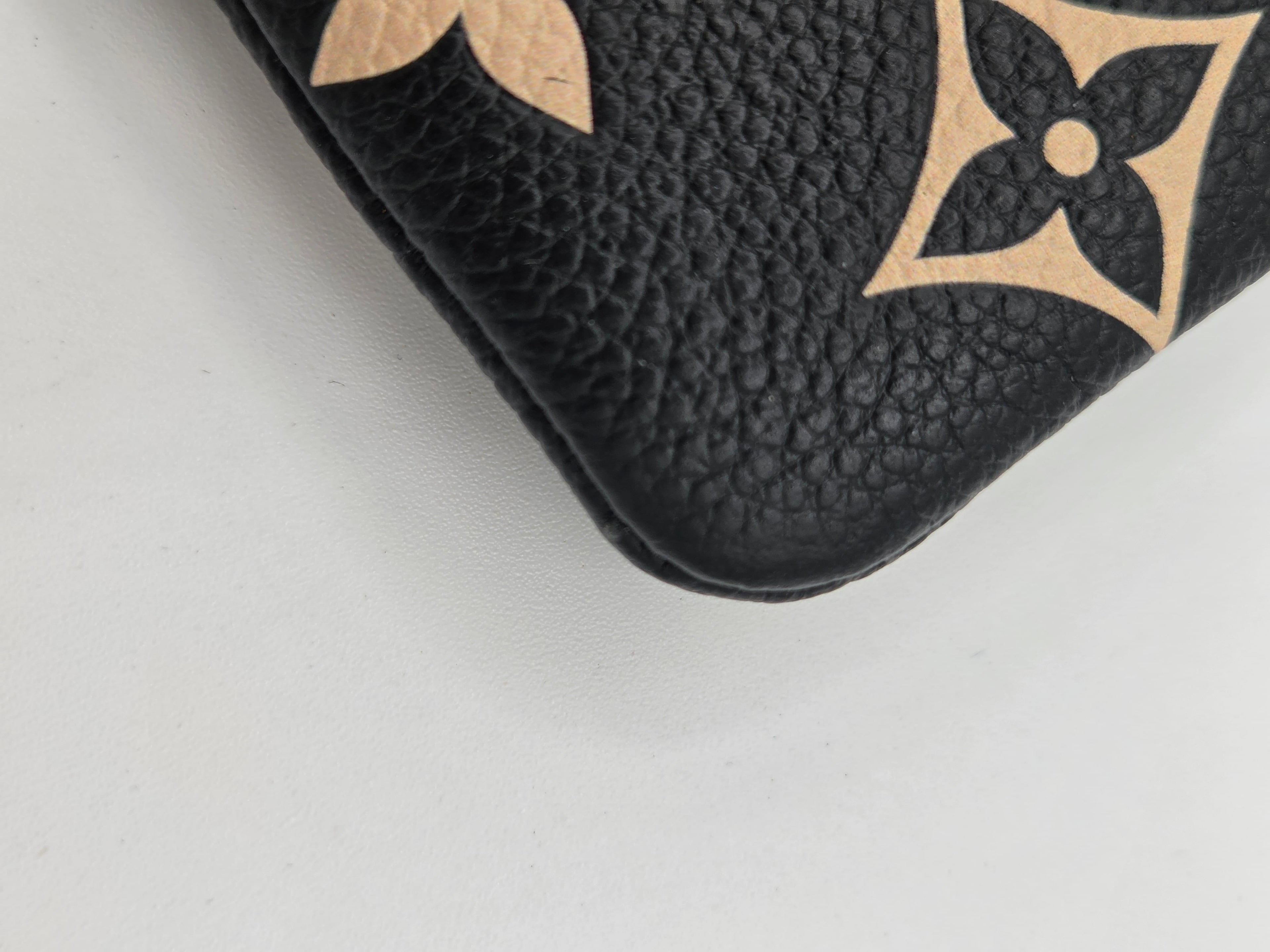 Close-up of a black pebbled leather item featuring a beige Louis Vuitton monogram pattern, showing the textured leather grain and part of the iconic flower motif.
