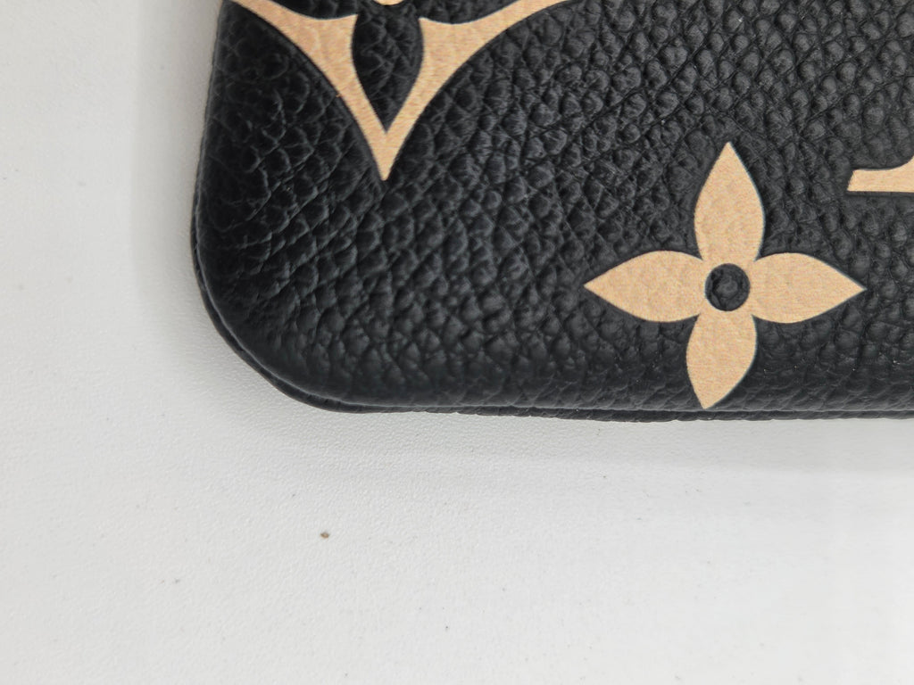 Close-up of a black textured leather item featuring the beige Louis Vuitton monogram pattern, including a floral motif and part of a letter V, on a white background.