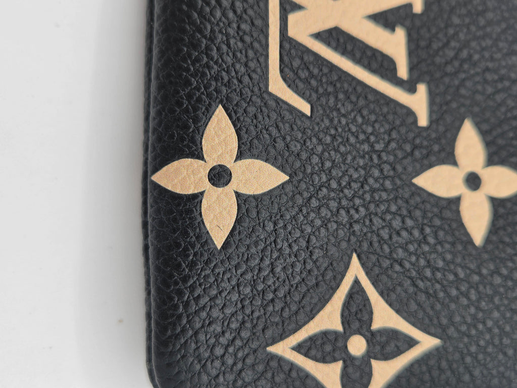 Close-up of a black pebbled leather Louis Vuitton monogram accessory featuring gold-tone printed monogram motifs and floral patterns.