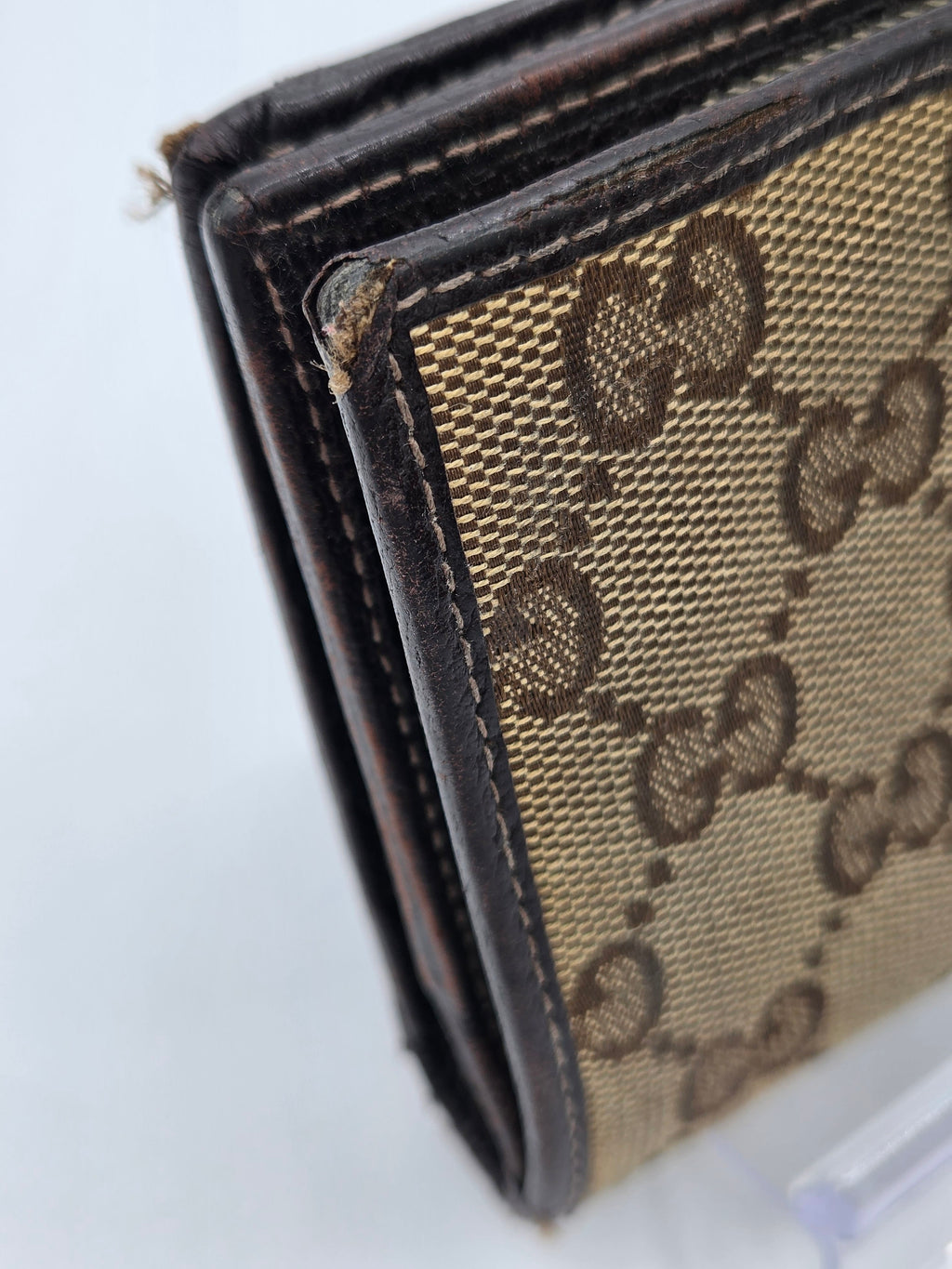 A close-up of a brown and beige monogram wallet, showing the classic interlocking G pattern on a canvas background with dark brown leather trim.