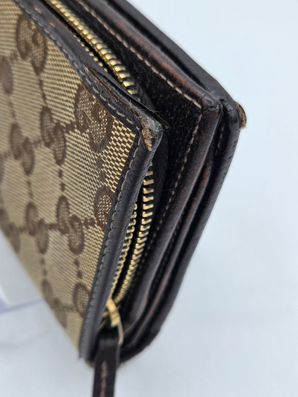 Close-up of a Gucci monogram canvas and leather zip-around wallet showing the classic GG pattern, dark brown leather trim, and gold-tone zipper.