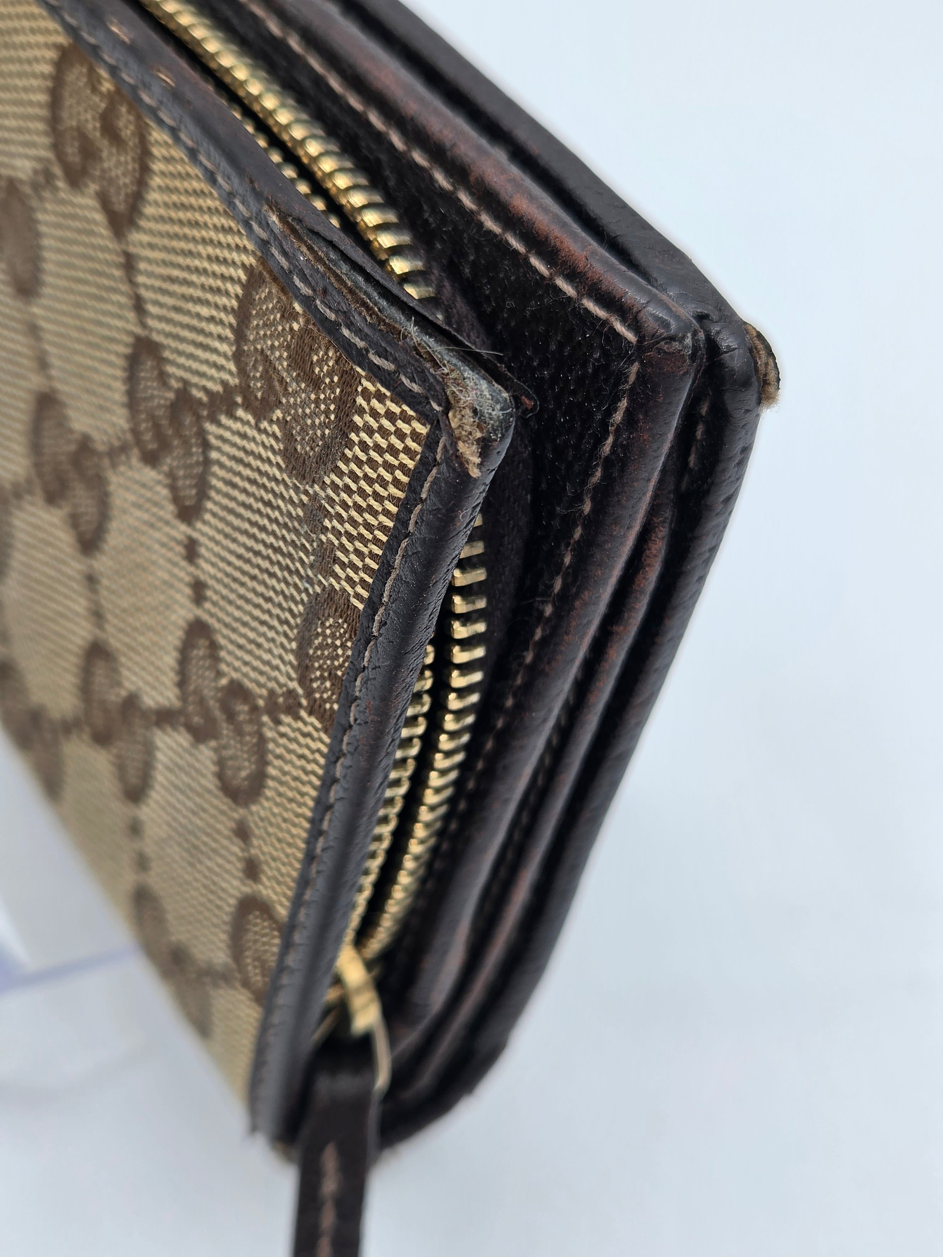 Close-up of a Gucci monogram canvas and leather zip-around wallet showing the classic GG pattern, dark brown leather trim, and gold-tone zipper.