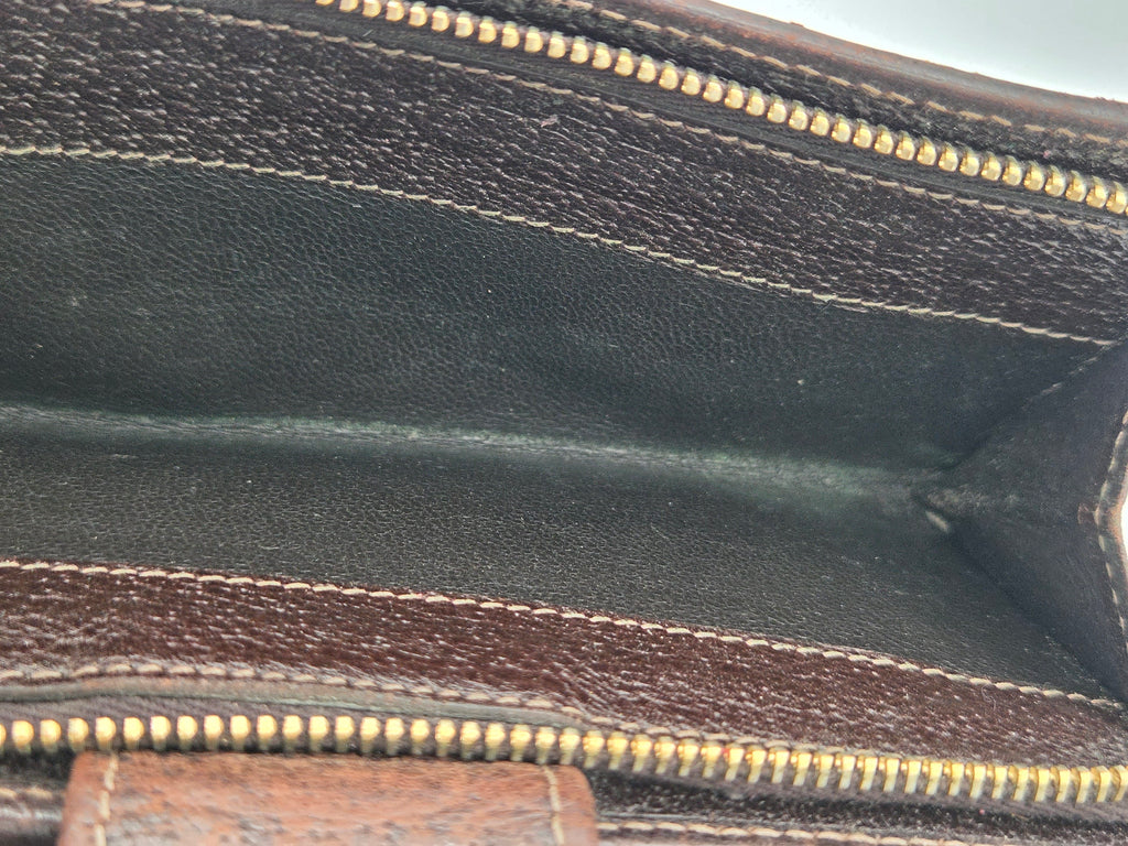 Close-up of the interior of a brown leather pouch or wallet, showing the dark brown inner lining, gold-toned zipper teeth, and contrast stitching.