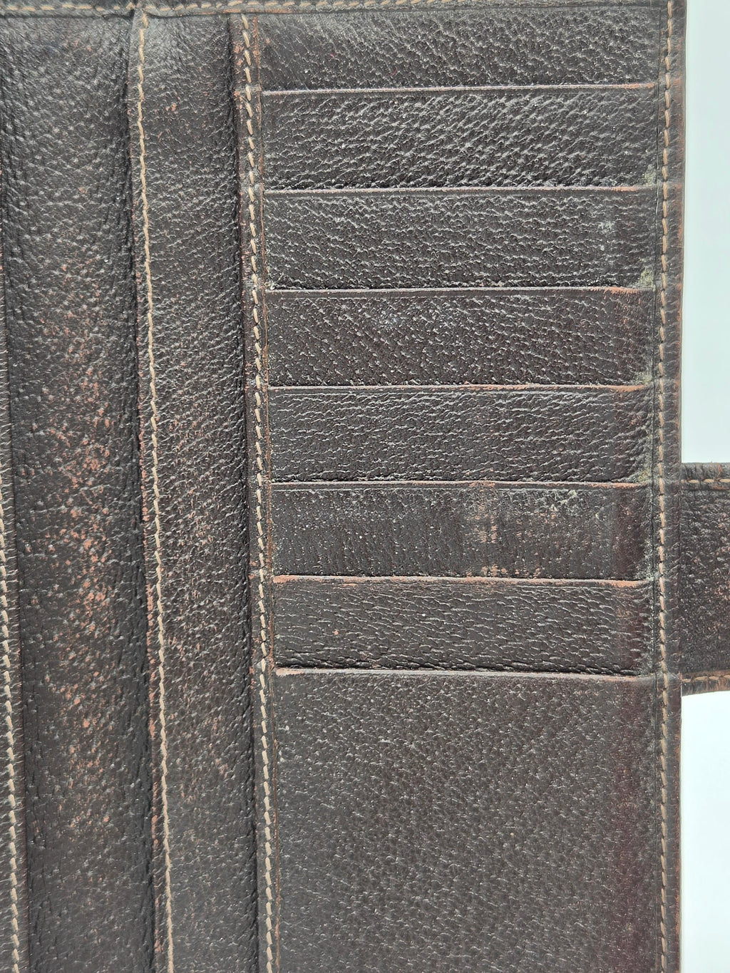 Close-up of a dark brown textured leather wallet showing card slots, stitching, and a pull tab.