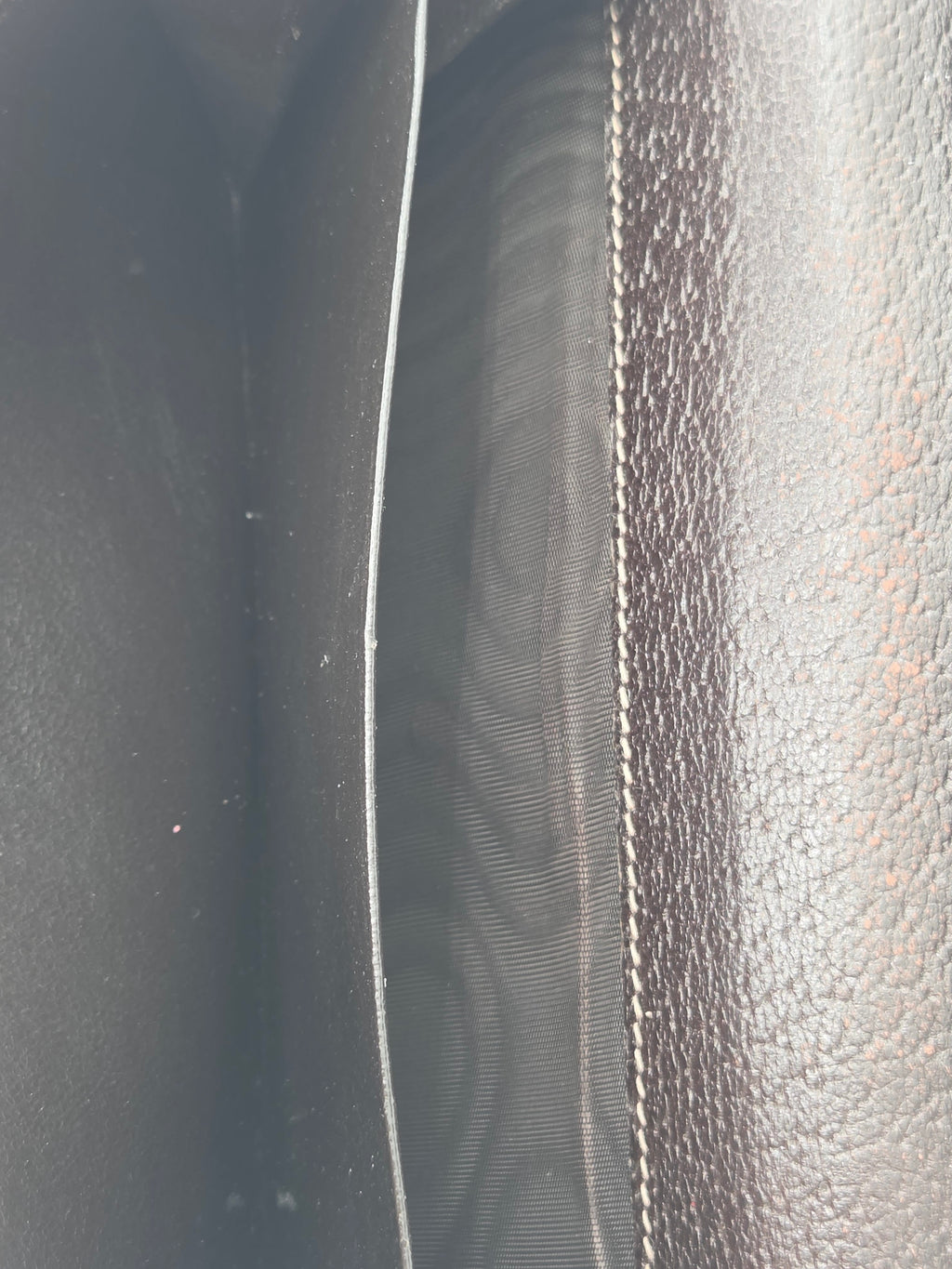 Close-up of a dark brown textured leather interior with white contrast stitching and a dark fabric lining.