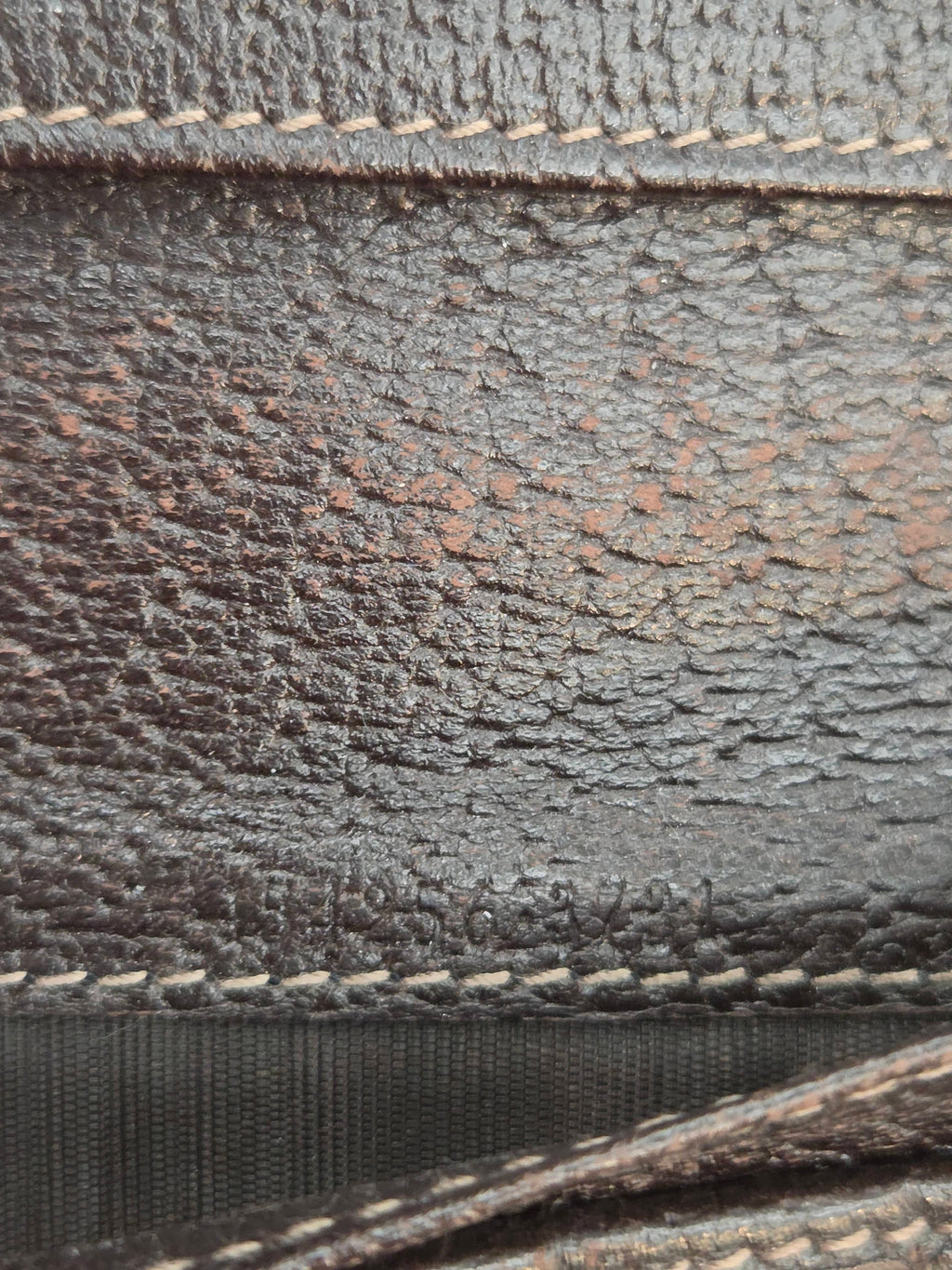 Close-up of a dark brown textured leather material with visible grain, contrast stitching, and a black woven strap.