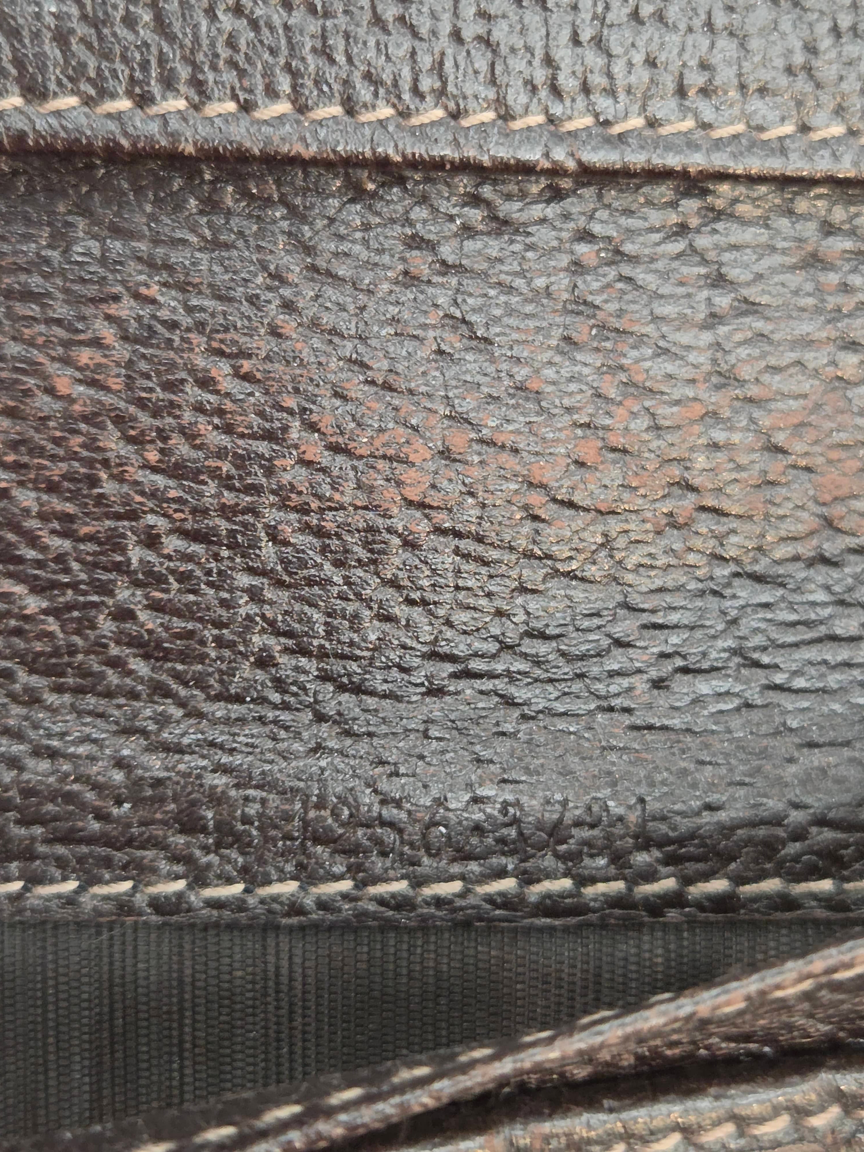 Close-up of a dark brown textured leather material with visible grain, contrast stitching, and a black woven strap.