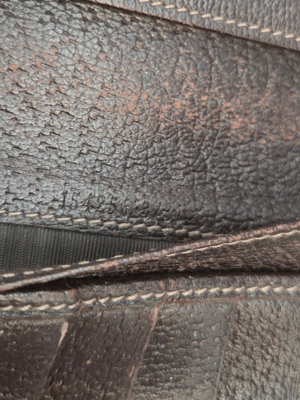 Close-up of dark brown textured leather with visible grain and contrast stitching along the edges.