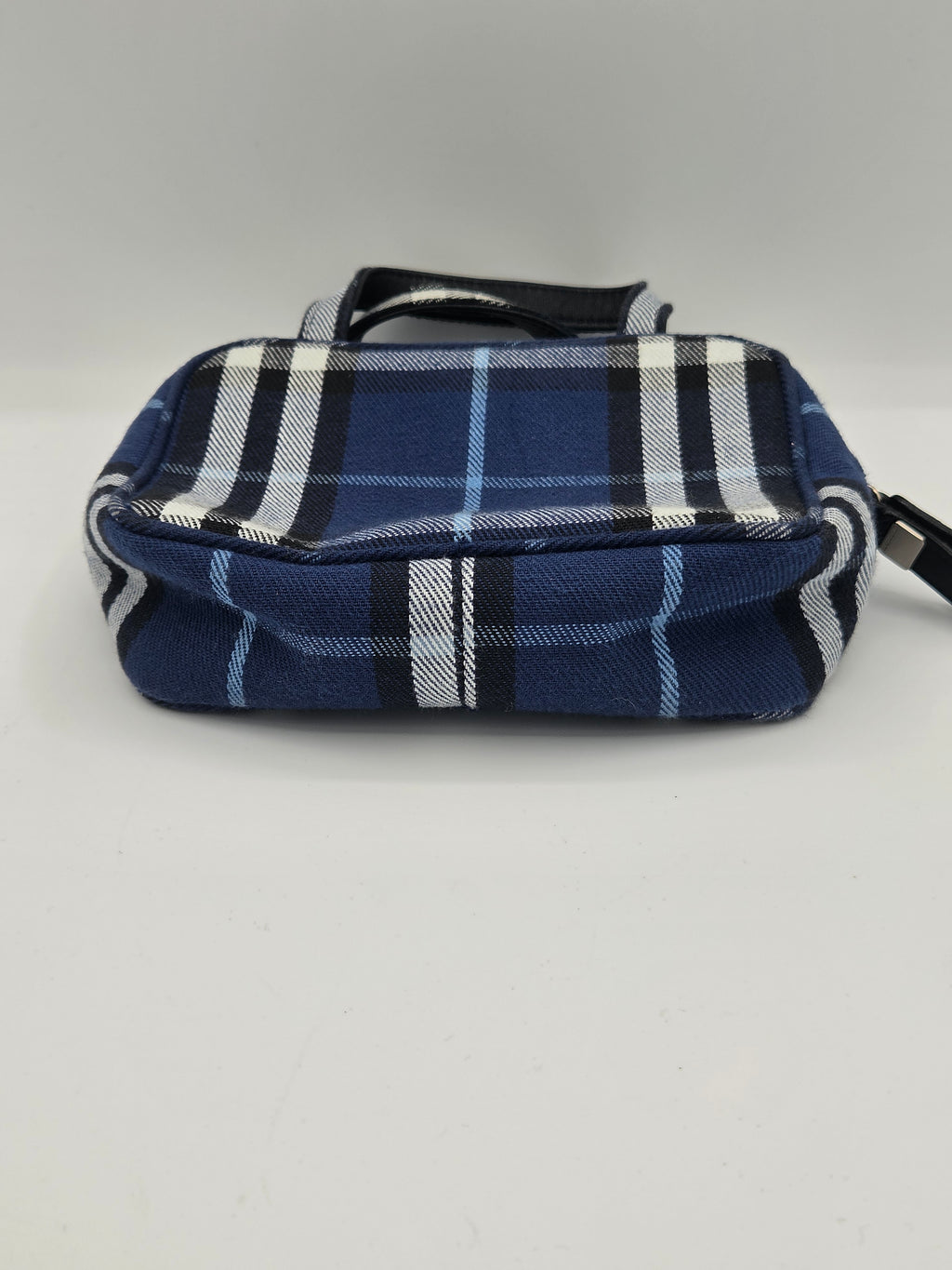 A small blue plaid pouch or bag with black and white stripes, hanging against a plain light gray wall.