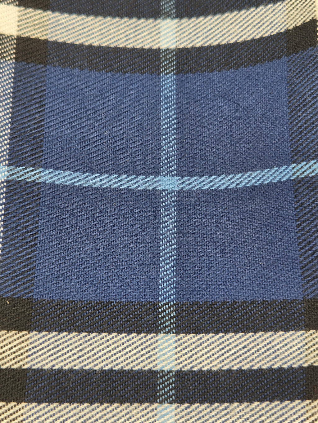 A close-up of a plaid fabric pattern featuring medium blue blocks, black and white vertical stripes, and thin light blue diagonal lines.