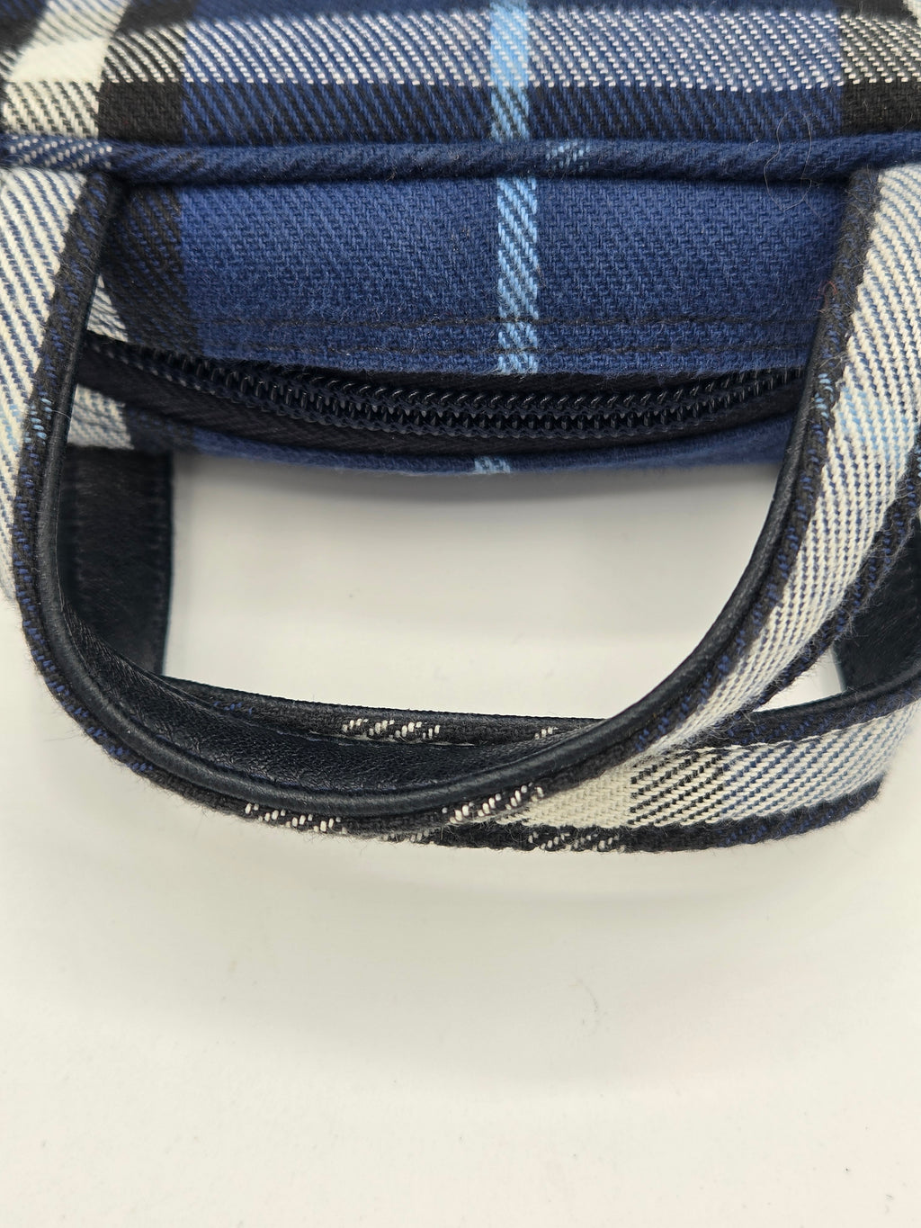Close-up of a plaid fabric zipper pouch in navy, blue, white, and black, showing the interior zipper and trim against a plain white background.