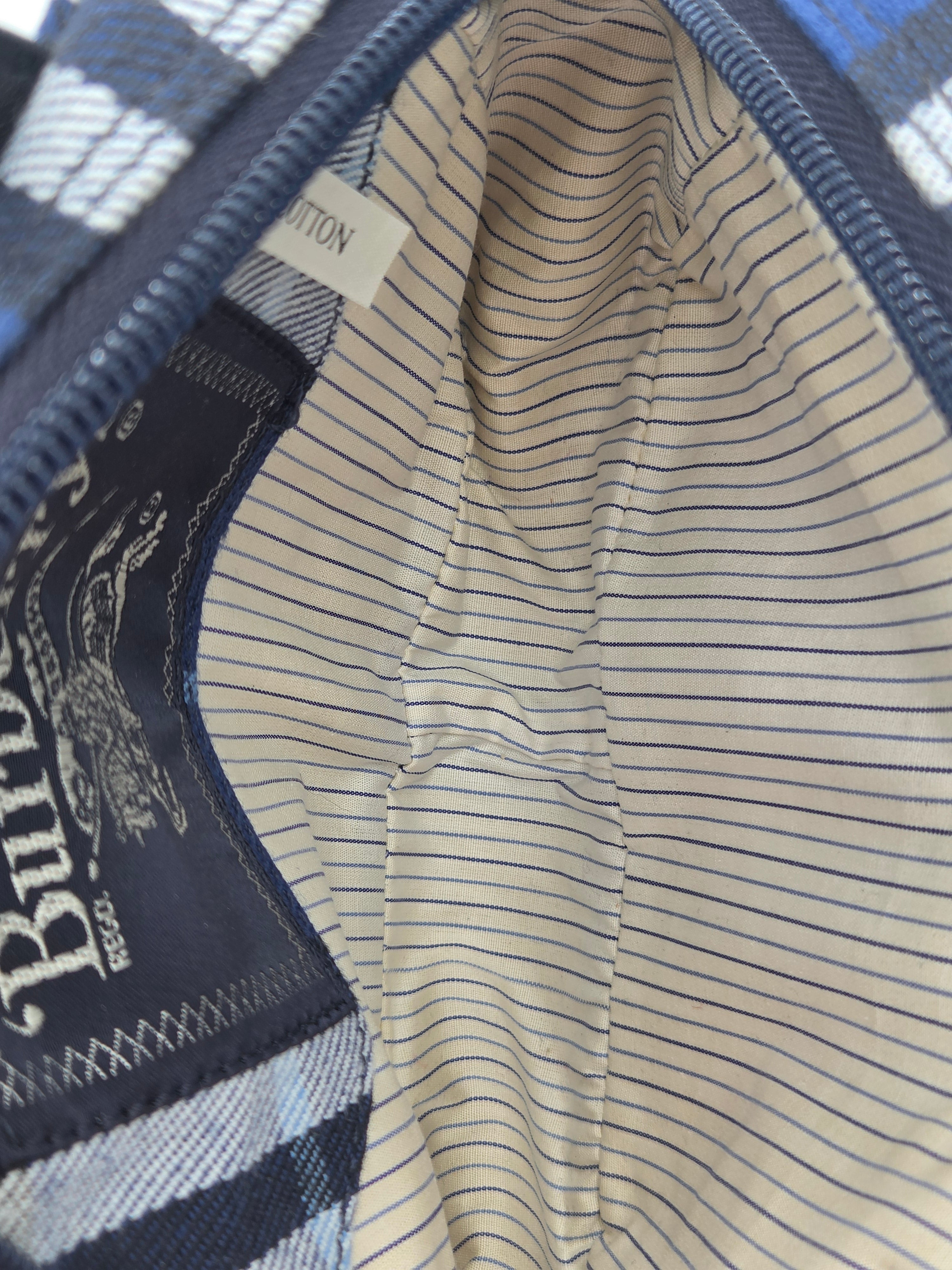 Close-up of a Burberry bag interior showing a cream pinstriped lining, a navy zipper, and a navy Burberry check fabric exterior edge with a visible Burberry logo patch.