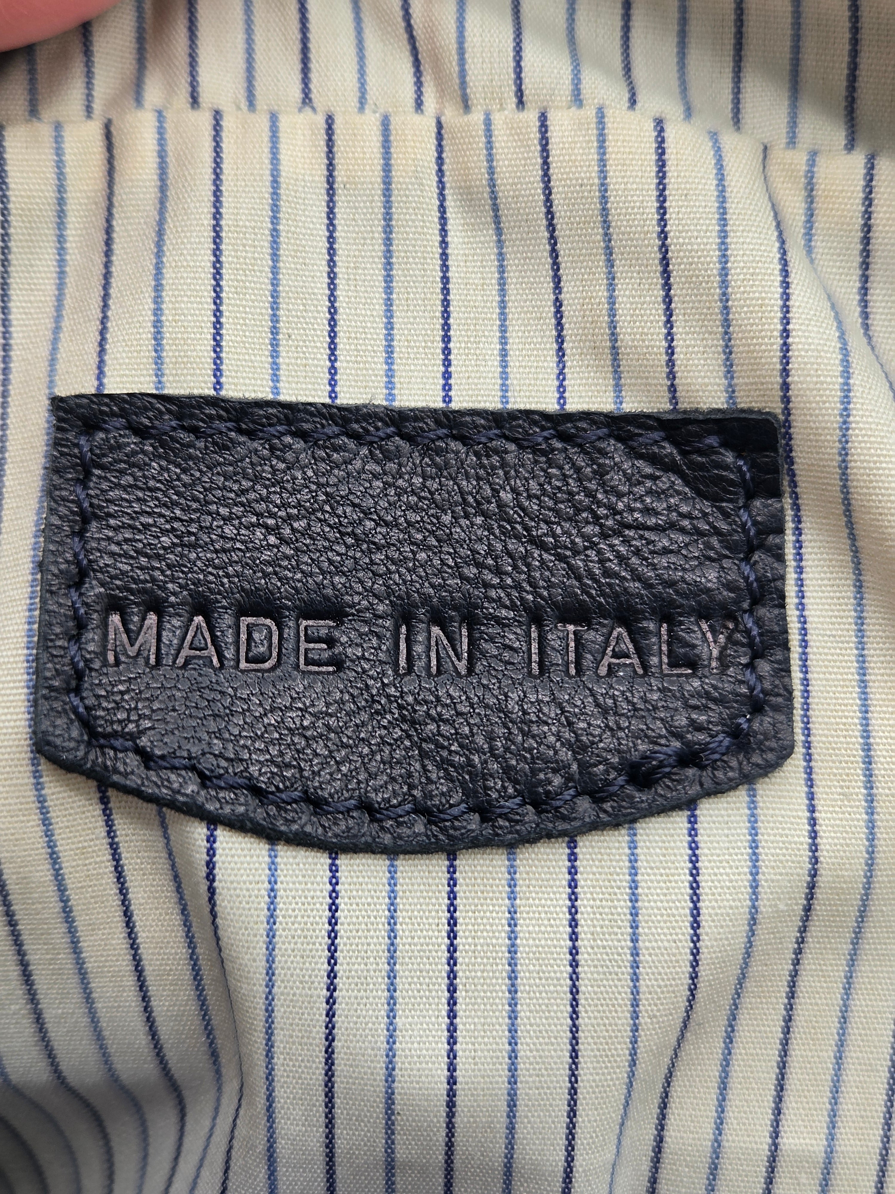 Close-up of a dark gray textured leather patch on a cream and blue striped fabric, featuring the text 'MADE IN ITALY' stitched vertically.