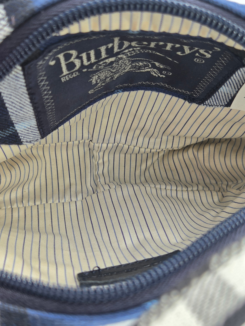 Close-up of the interior of a Burberry bag, showing a navy blue zipper, a cream and navy striped lining, and a visible Burberry brand label.